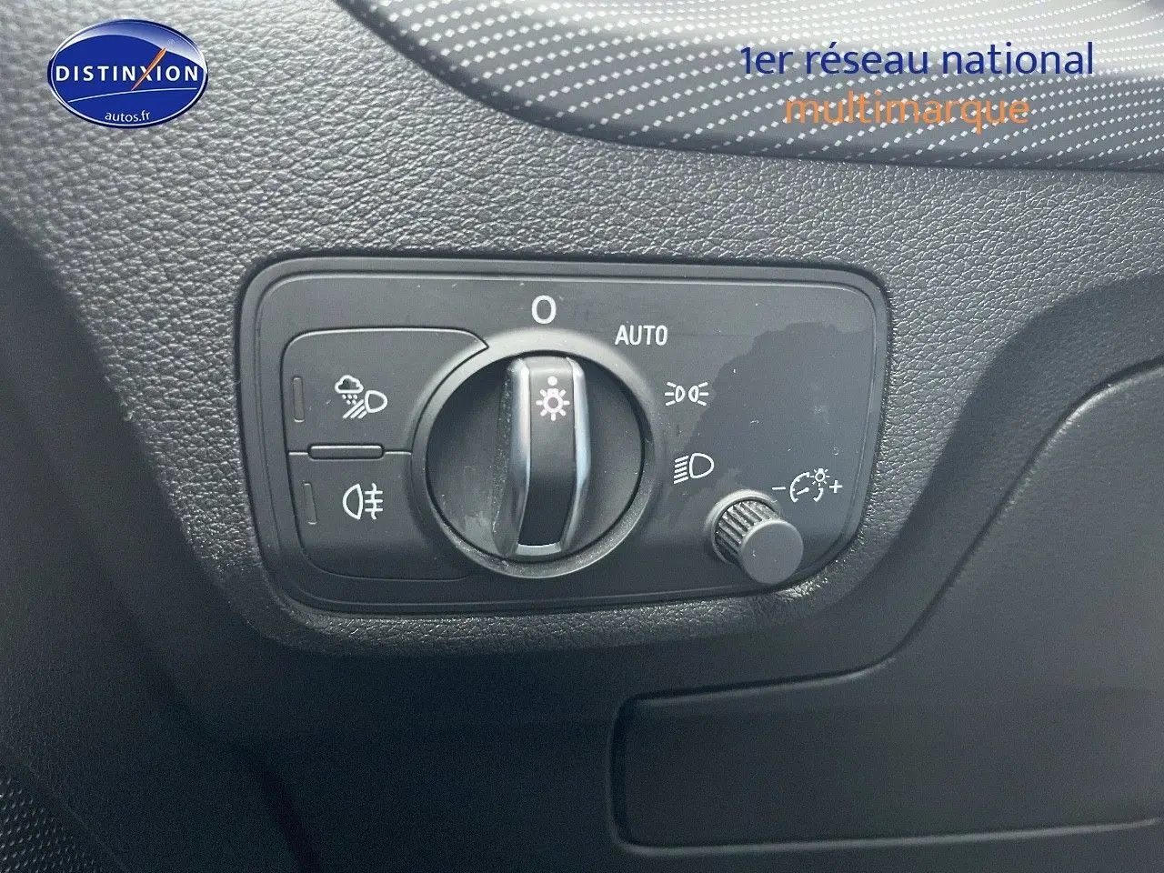 Commande des phares en gros plan sur le tableau de bord noir d’un Audi Q2 blanc, avec réglage automatique et antibrouillard.