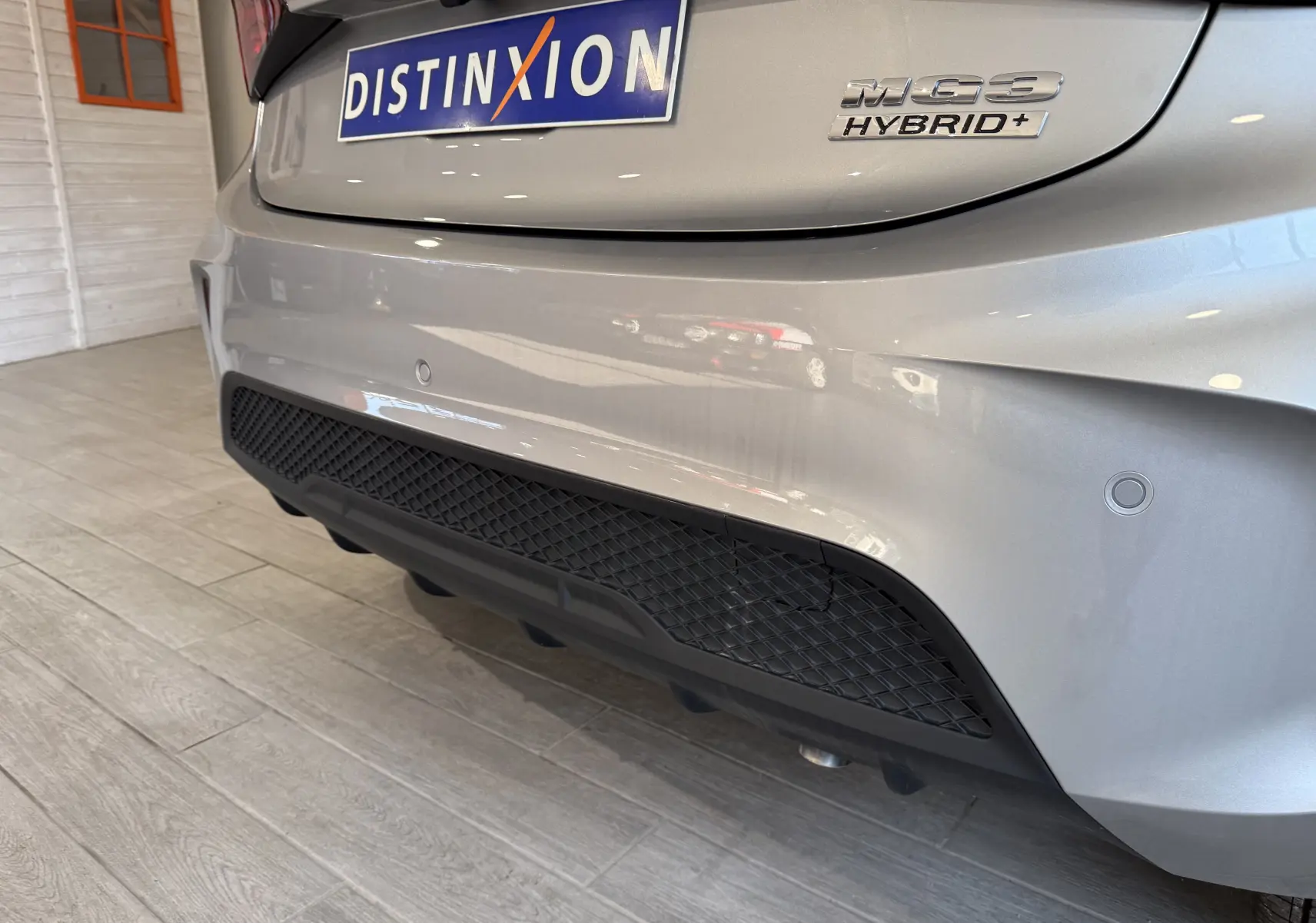 Gros plan sur l’arrière droit du MG3 Cosmic Silver 1.5 L Hybrid+ avec logo et diffuseur noir en intérieur showroom.