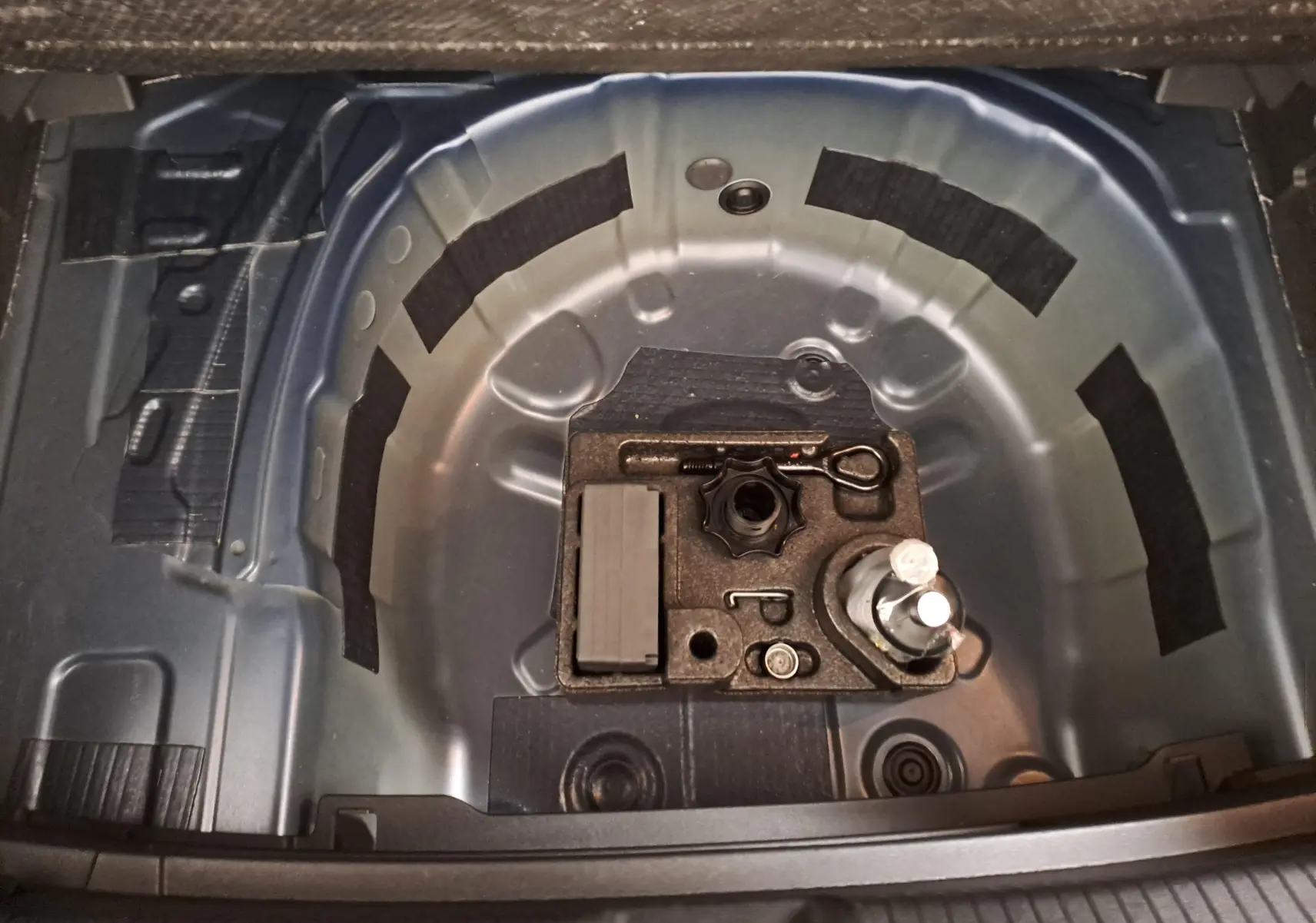 Vue en plongée sur le coffre ouvert d'une Volkswagen Polo bleu récif, montrant le rangement pour roue de secours et outils.