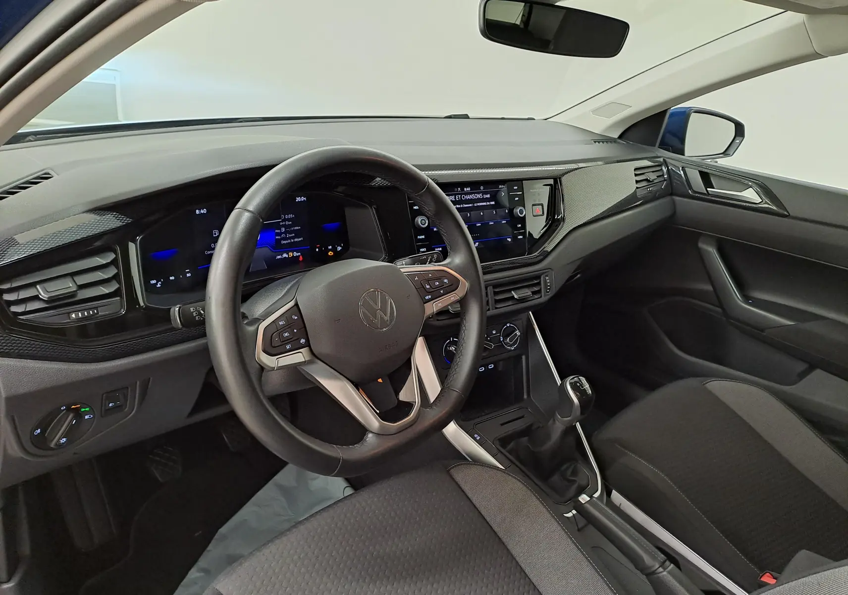 Vue intérieure côté conducteur de la Volkswagen Polo 2025, tableau de bord noir avec volant cuir multifonctions et écran tactile central.