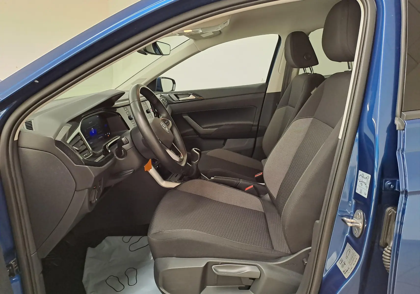 Vue côté gauche de l'intérieur bleu récif d'une Volkswagen Polo 2025, sièges avant gris et volant cuir multifonctions.