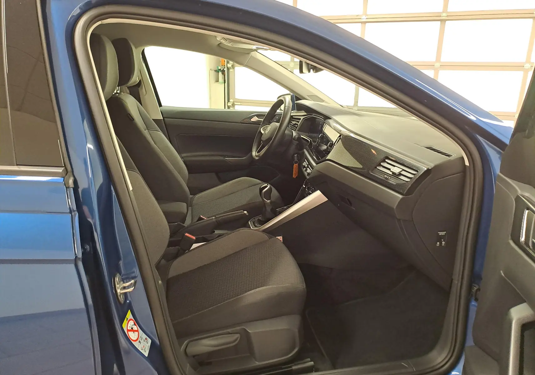 Vue intérieure côté gauche de la Volkswagen Polo Bleu Récif 2025, montrant sièges tissu noirs et tableau de bord moderne.