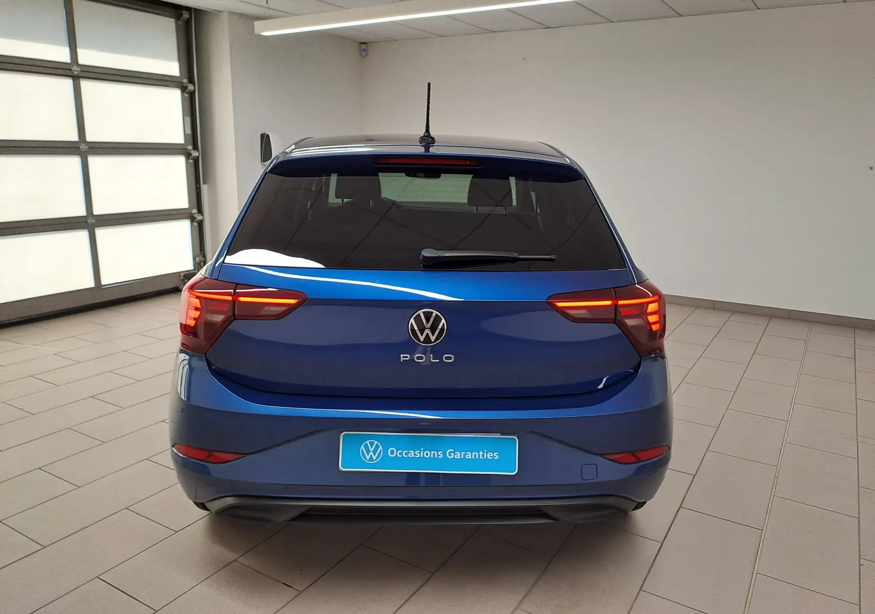Vue arrière d'une Volkswagen Polo 2025 Bleu Récif avec feux arrière LED allumés dans un garage lumineux.
