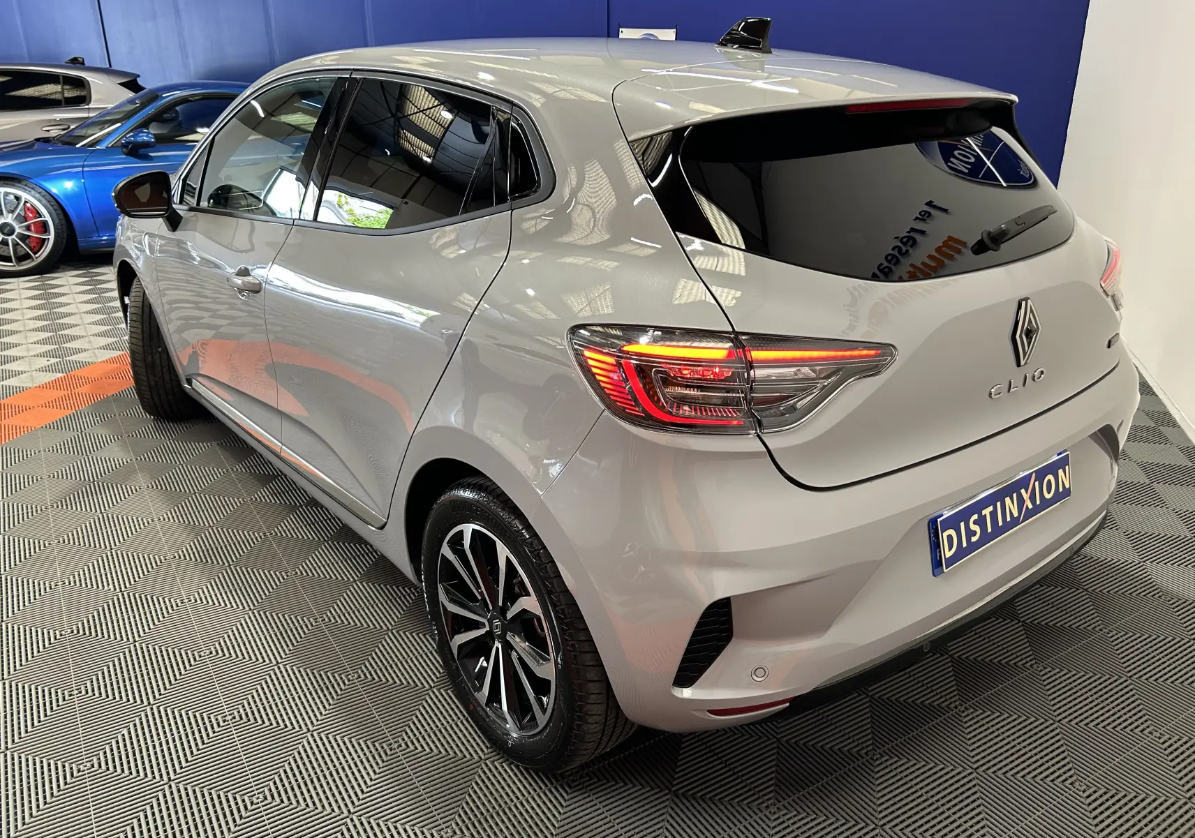 Vue 3/4 arrière droite d’une Renault Clio V E-Tech gris Rafale métallisé avec feux arrière allumés en intérieur showroom.