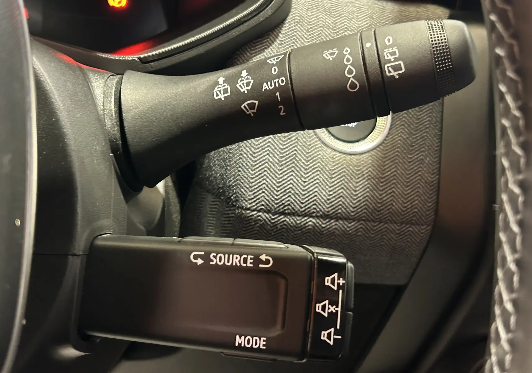 Gros plan sur les commandes au volant de la Renault Clio V hybride, avec motifs gris et boutons de réglage audio visibles.