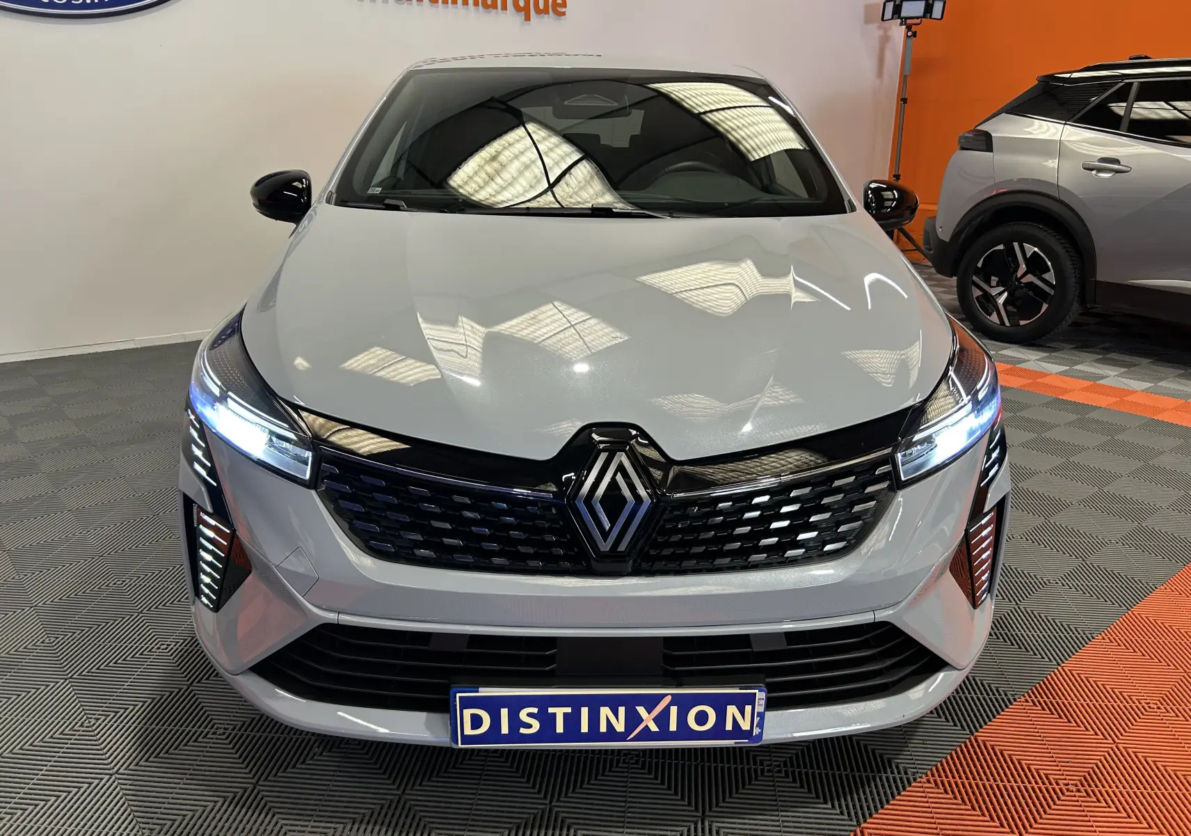 Vue avant d'une Renault Clio V E-Tech Full Hybrid gris rafale métal avec phares allumés dans un showroom.