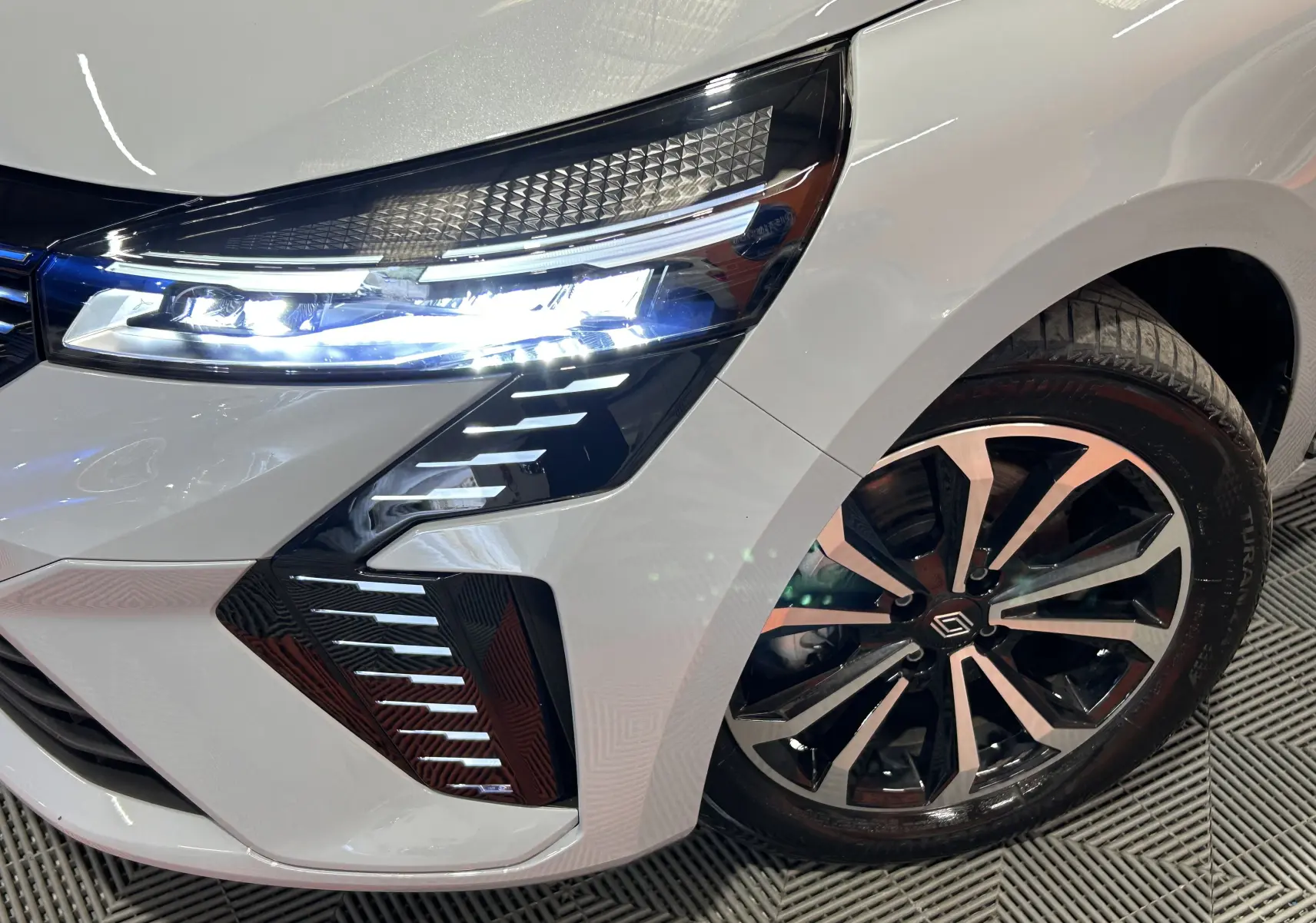 Gros plan sur l'avant droit gris rafale métal de la Renault Clio V E-Tech, mettant en valeur le phare LED et la jante alliage.
