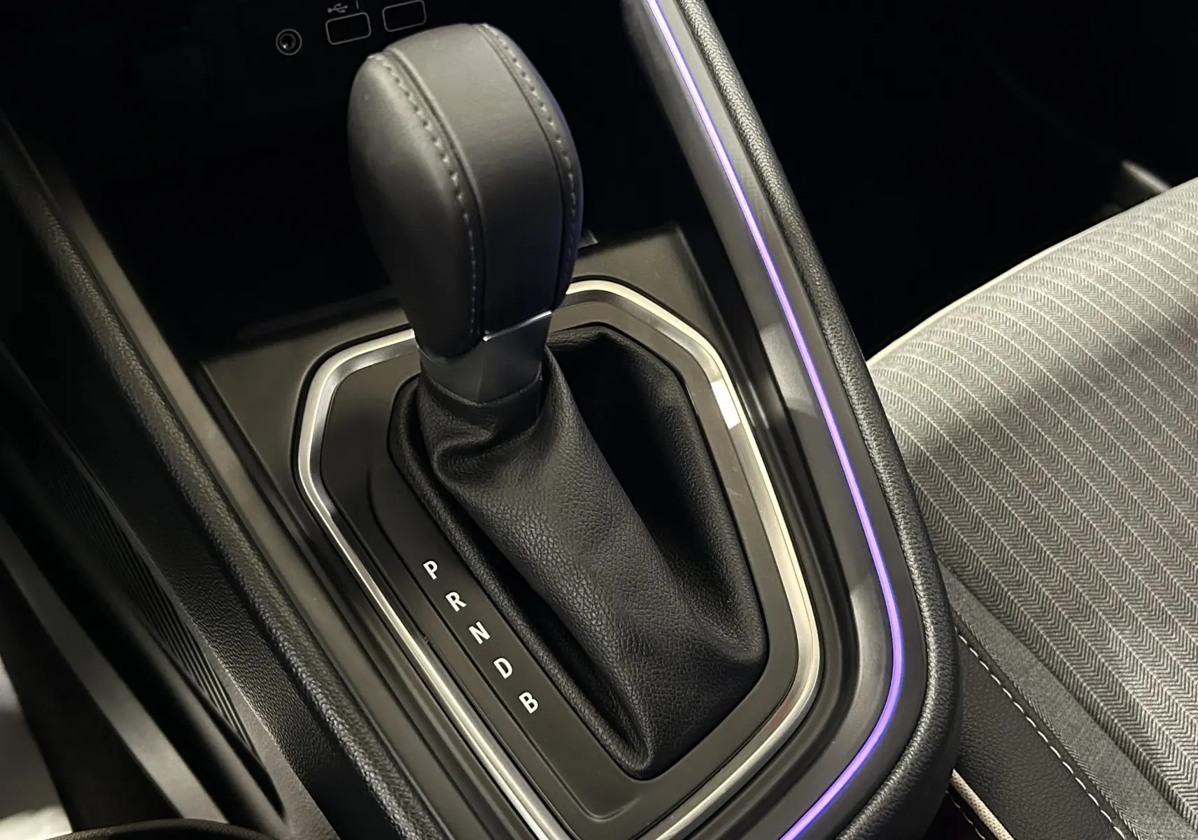 Le levier de vitesses automatique noir de la Renault Clio V E-Tech, avec éclairage d'ambiance violet et tissu gris à motifs.