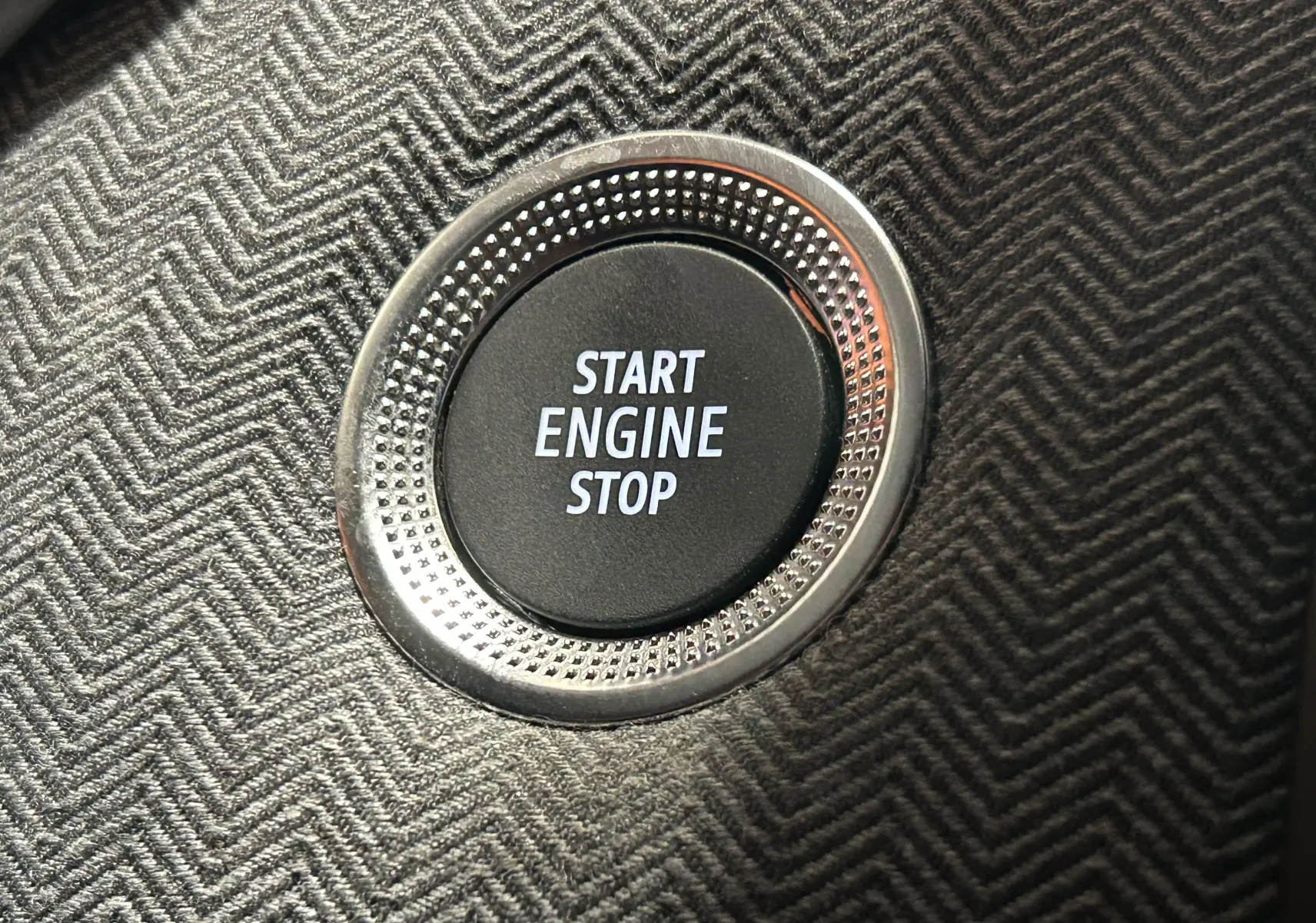 Bouton Start Engine Stop en gros plan sur la console intérieure au tissu gris à motif chevron de la Renault Clio V hybride.