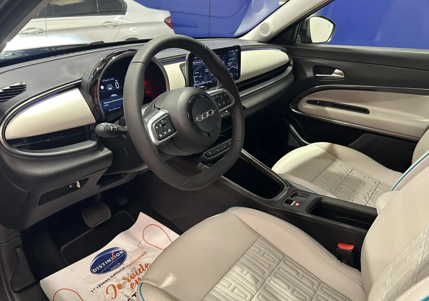 Intérieur clair de la Fiat 600 Hybrid 2024 vu côté conducteur, avec tableau de bord moderne et sièges cuir chauffants.