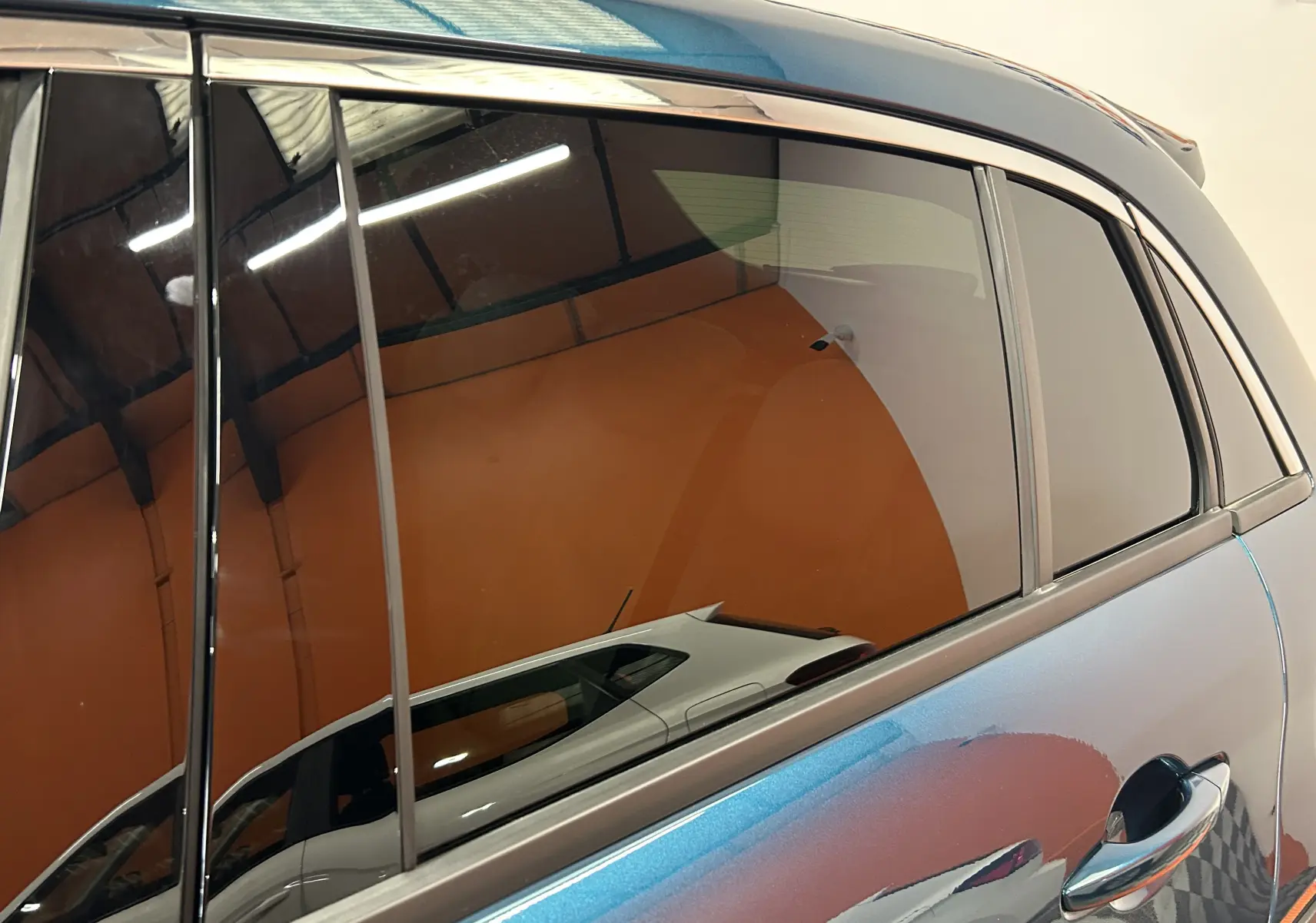 Gros plan sur la porte arrière droite bleu métallisé d'une FIAT 600 Hybrid 2024, avec reflet d'un autre véhicule blanc.