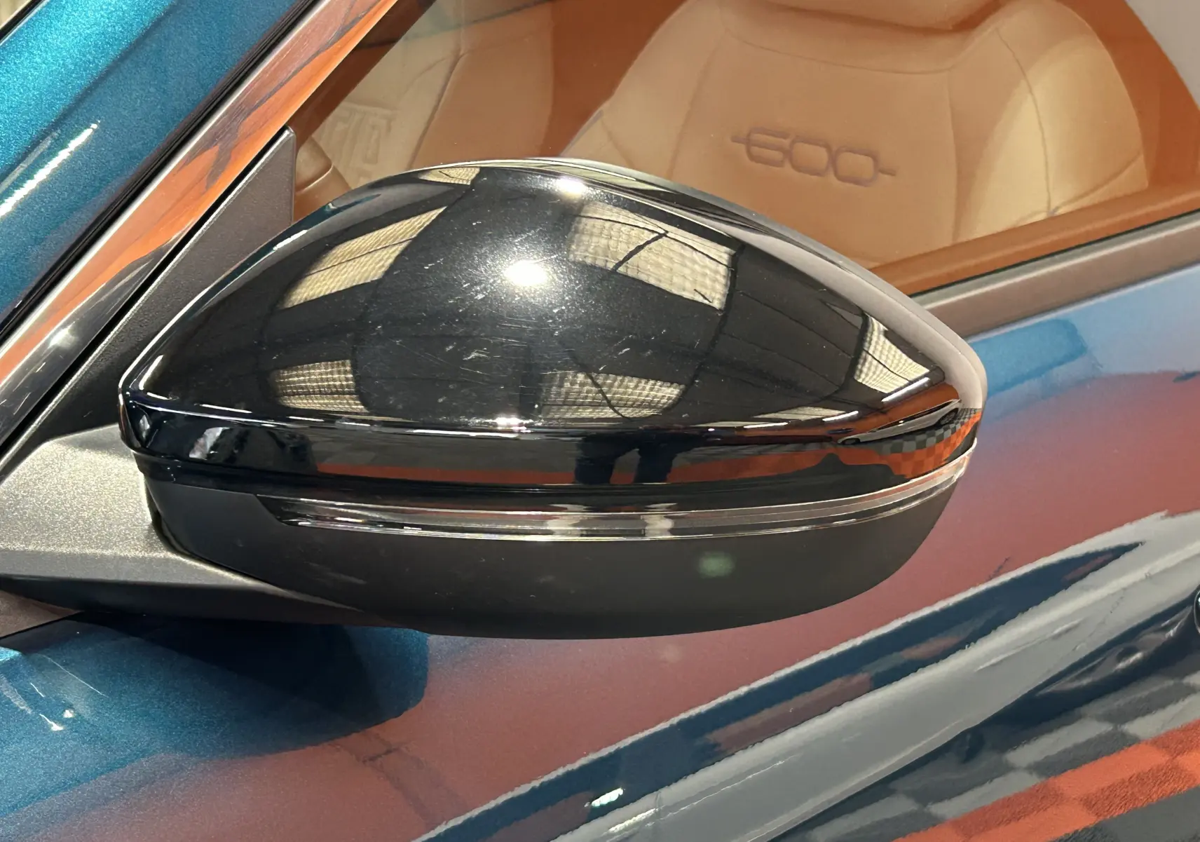 Rétroviseur noir côté gauche d'une FIAT 600 Hybrid 100 La Prima bleu avec intérieur cuir marron visible en arrière-plan.