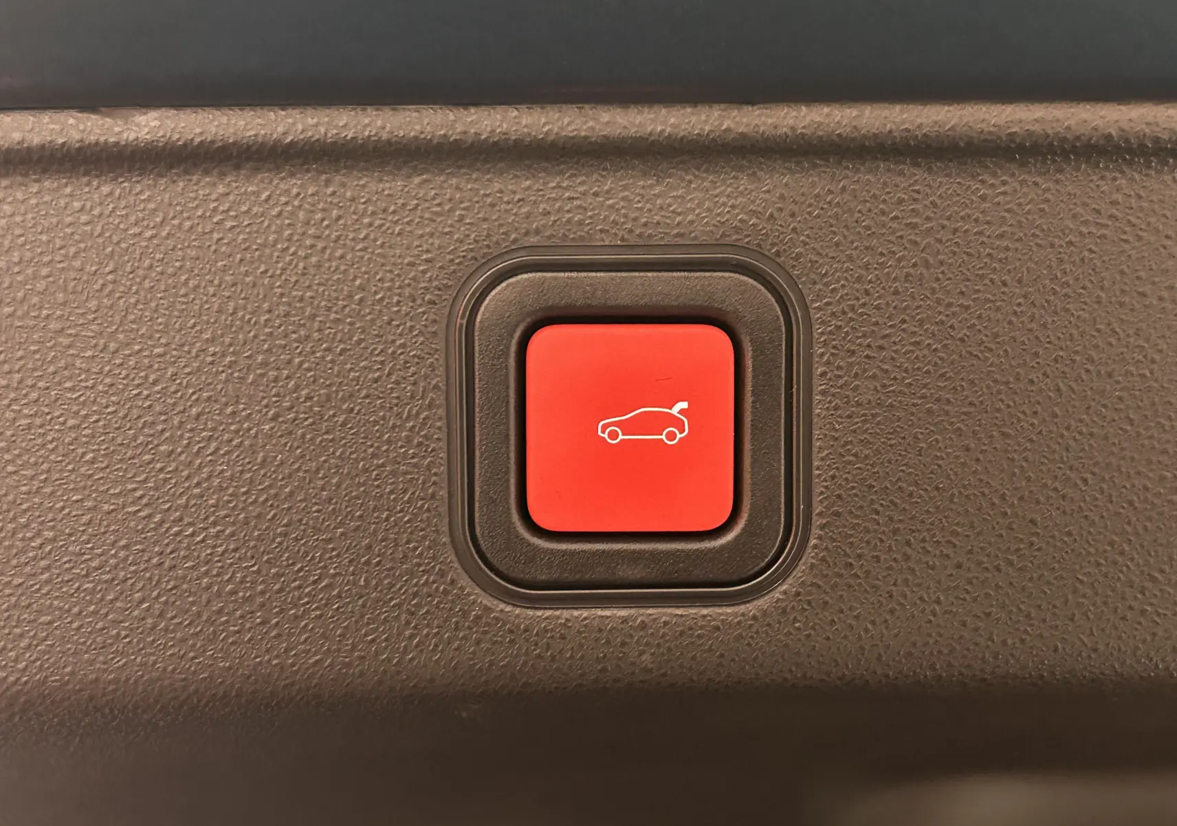 Bouton rouge d'ouverture électrique du hayon sur la planche intérieure d'une FIAT 600 Hybrid 2024 bleu.