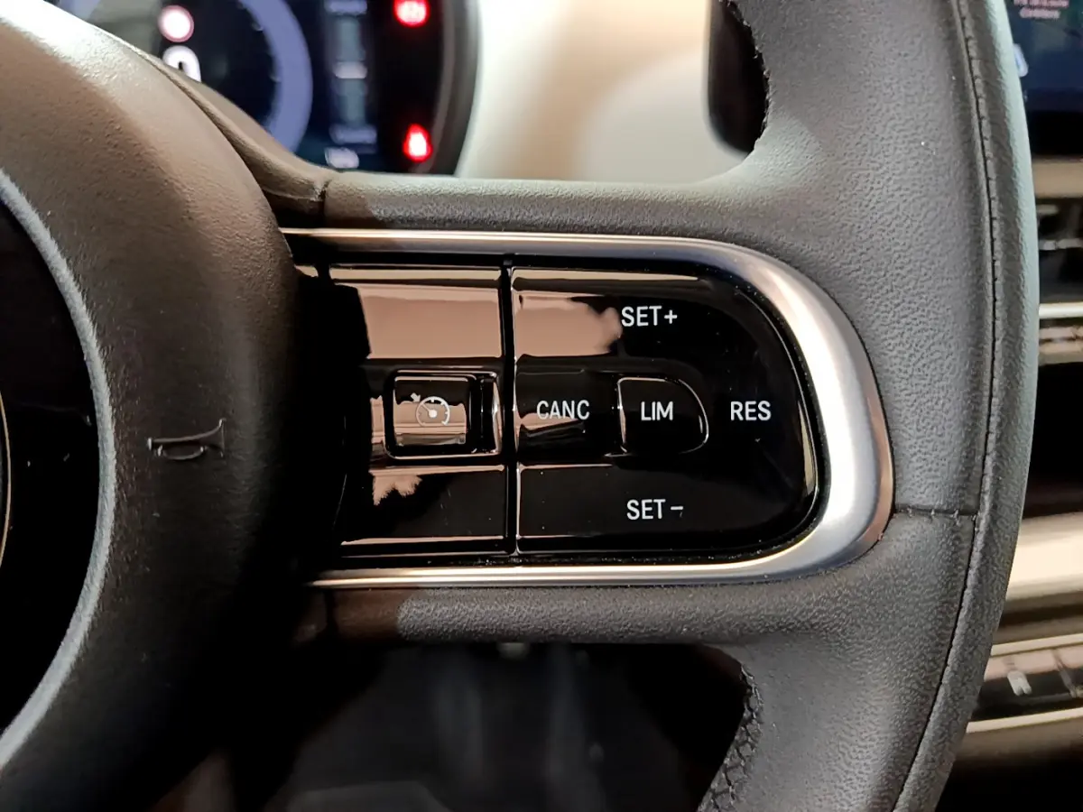 Gros plan sur les commandes du régulateur de vitesse au volant cuir noir de la Fiat 500 blanche Icône 2022.