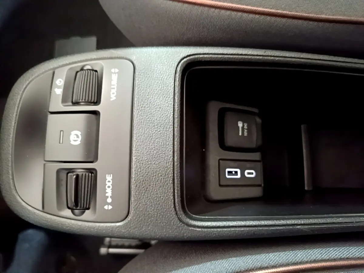 Gros plan sur la console centrale noire de la Fiat 500 électrique blanche, montrant commandes volume, mode et ports USB.