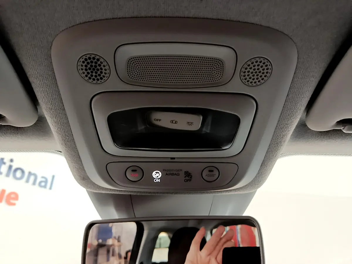 Vue intérieure du plafonnier gris clair avec commandes SOS et assist, rétroviseur et main visible dans une Fiat 500 blanche électrique.