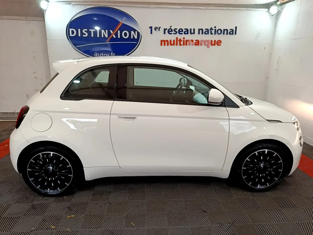 Profil droit d'une FIAT 500 électrique blanche 42kWh Icône 2022 avec jantes noires en intérieur showroom.