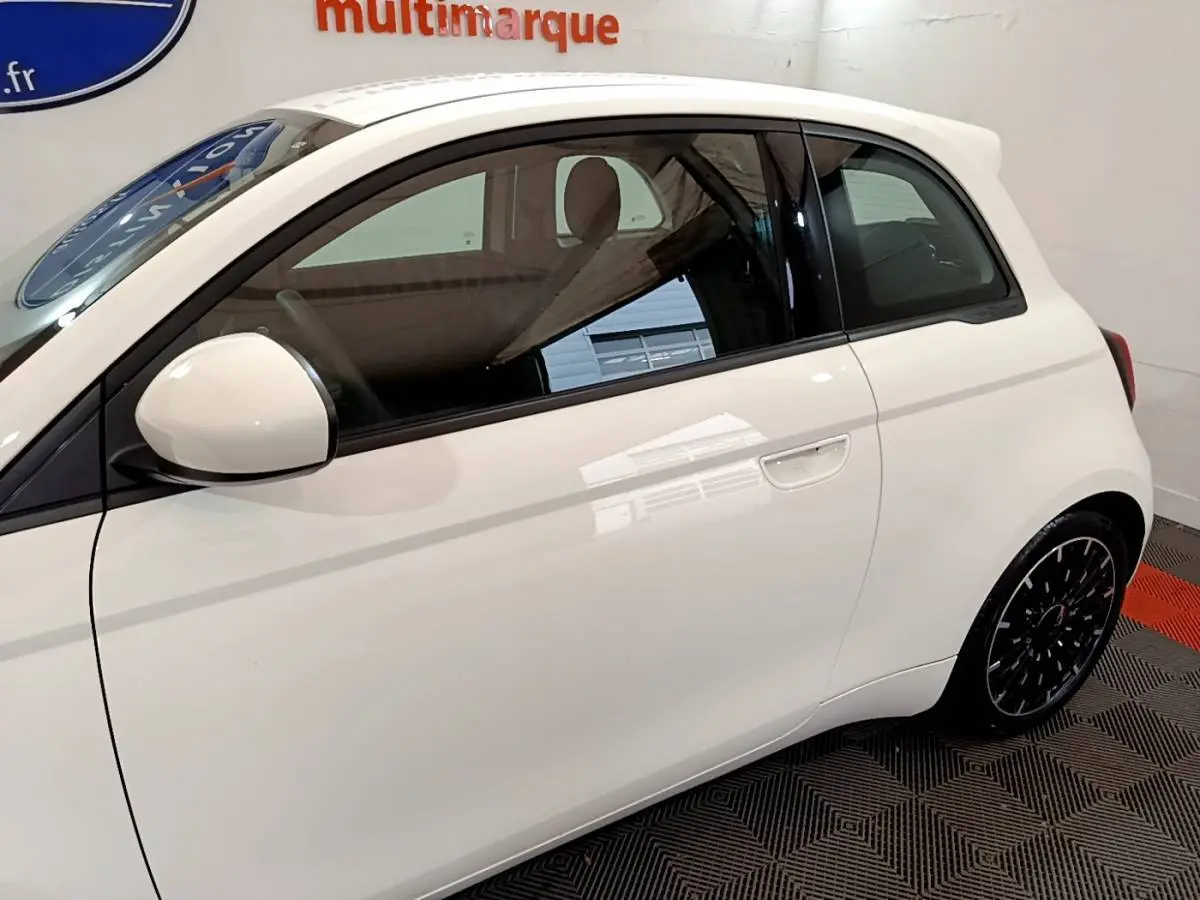Profil côté gauche de la FIAT 500 Icône électrique blanche, avec jantes noires et intérieur beige visible.