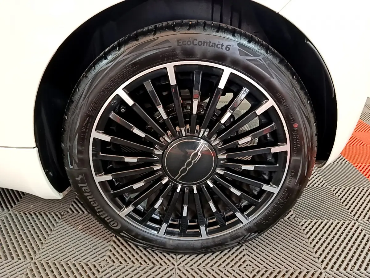 Gros plan sur la roue avant gauche de la FIAT 500 électrique blanche, mettant en valeur la jante noire à rayons fins.