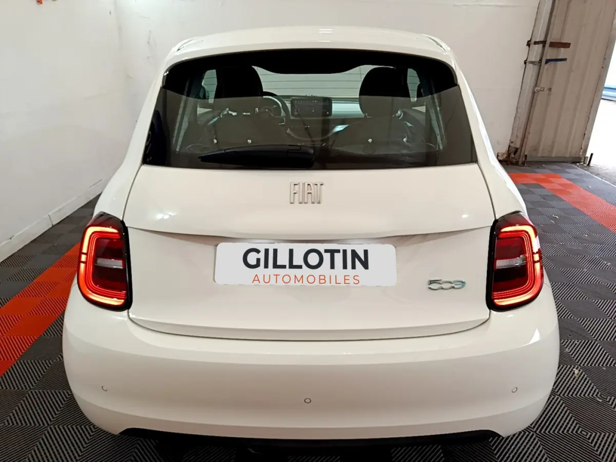 Vue arrière d'une Fiat 500 électrique blanche avec feux LED allumés dans un garage fermé.