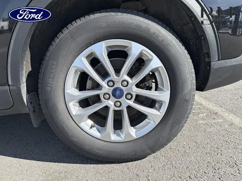 Gros plan sur la roue avant droite du Ford Kuga noir Agate, jante alu 17 pouces avec logo Ford central.