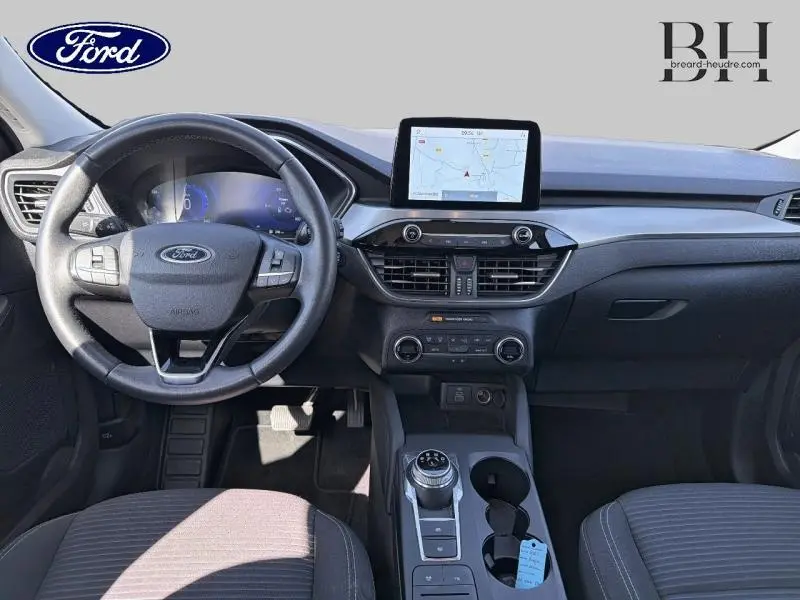 Vue intérieure avant du Ford Kuga 2023 avec volant cuir multifonction et écran tactile GPS au centre du tableau de bord.