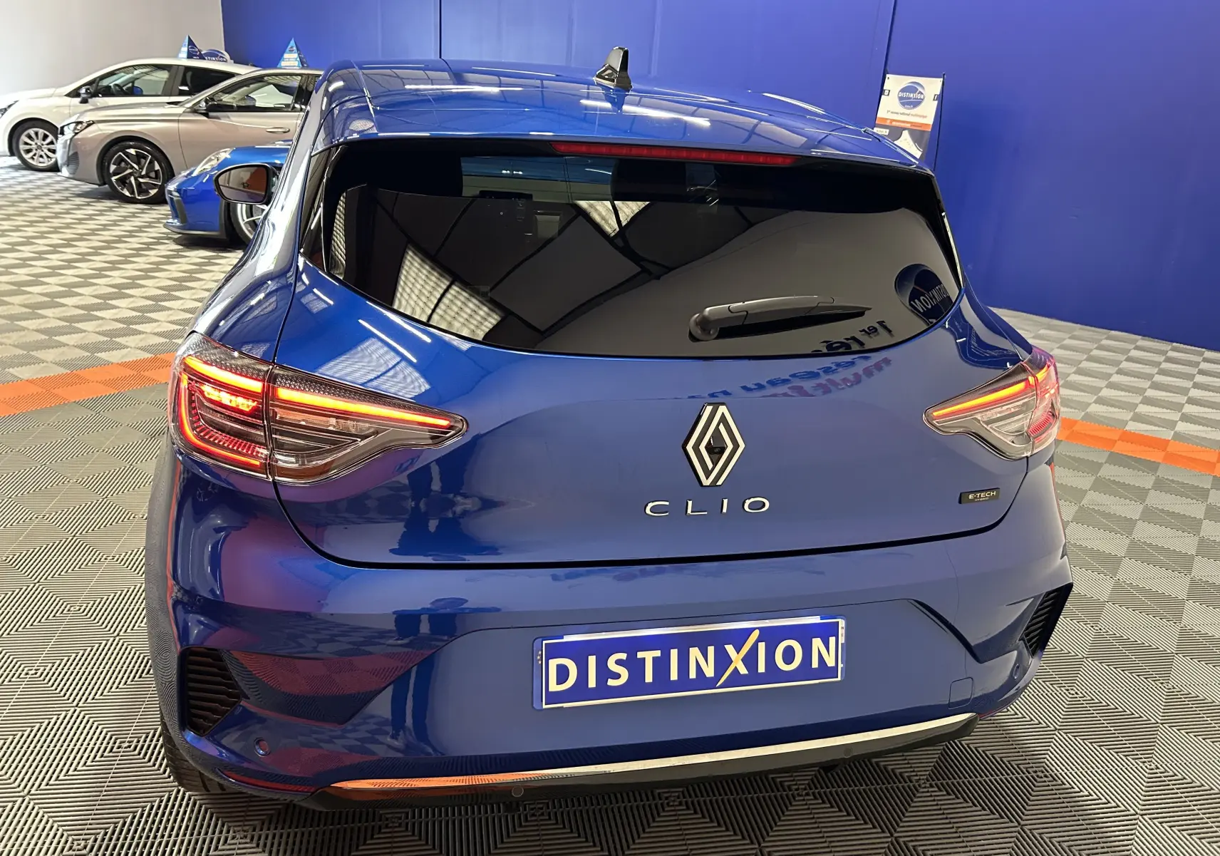 Vue arrière d'une Renault Clio V bleu iron metal avec feux LED allumés dans un showroom.