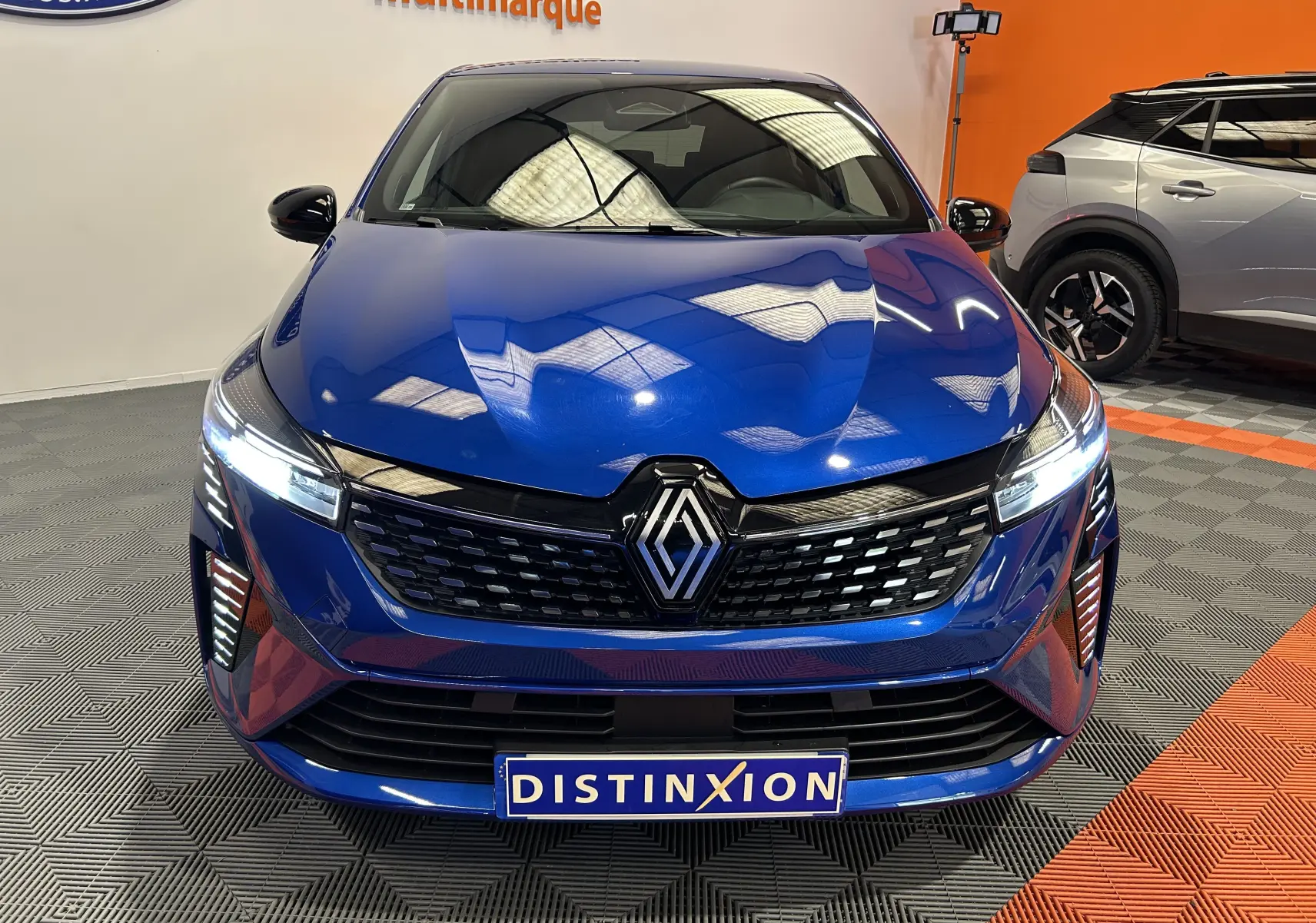 Vue avant d'une Renault Clio V E-Tech Full Hybrid 145 en bleu Iron Metal avec calandre noire et feux LED allumés.