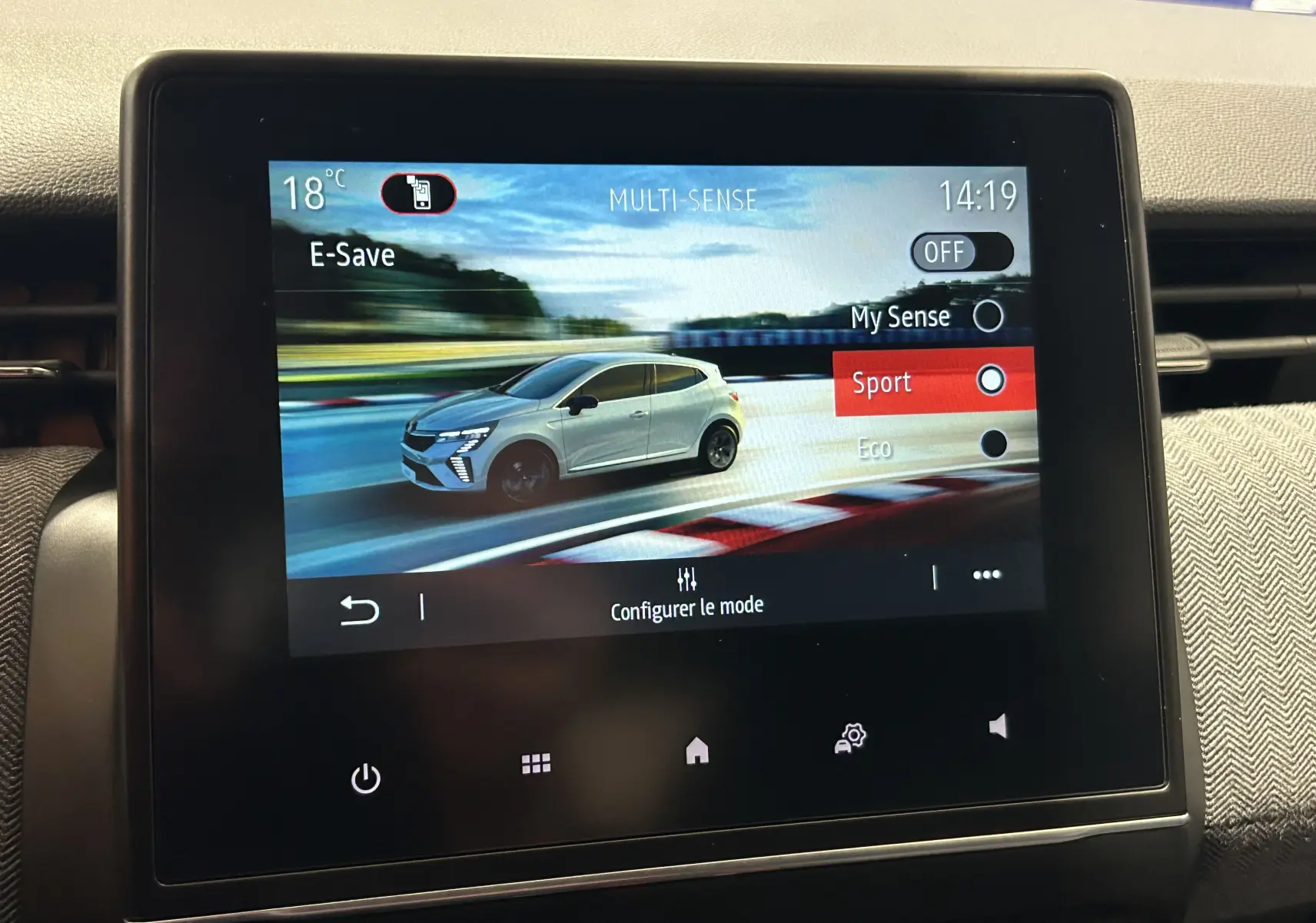 Écran tactile affichant un mode de conduite avec une Renault Clio V blanche en vue latérale droite sur circuit.