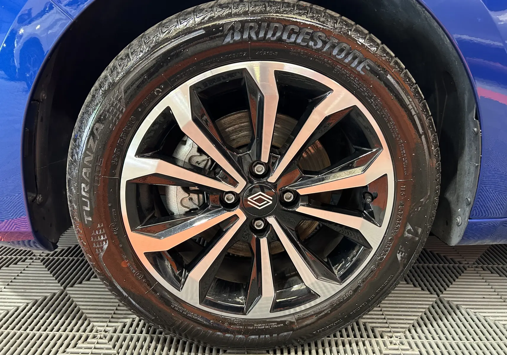 Gros plan sur la roue avant gauche de la Renault Clio V bleu Iron Metal avec jante alliage noire et argentée.
