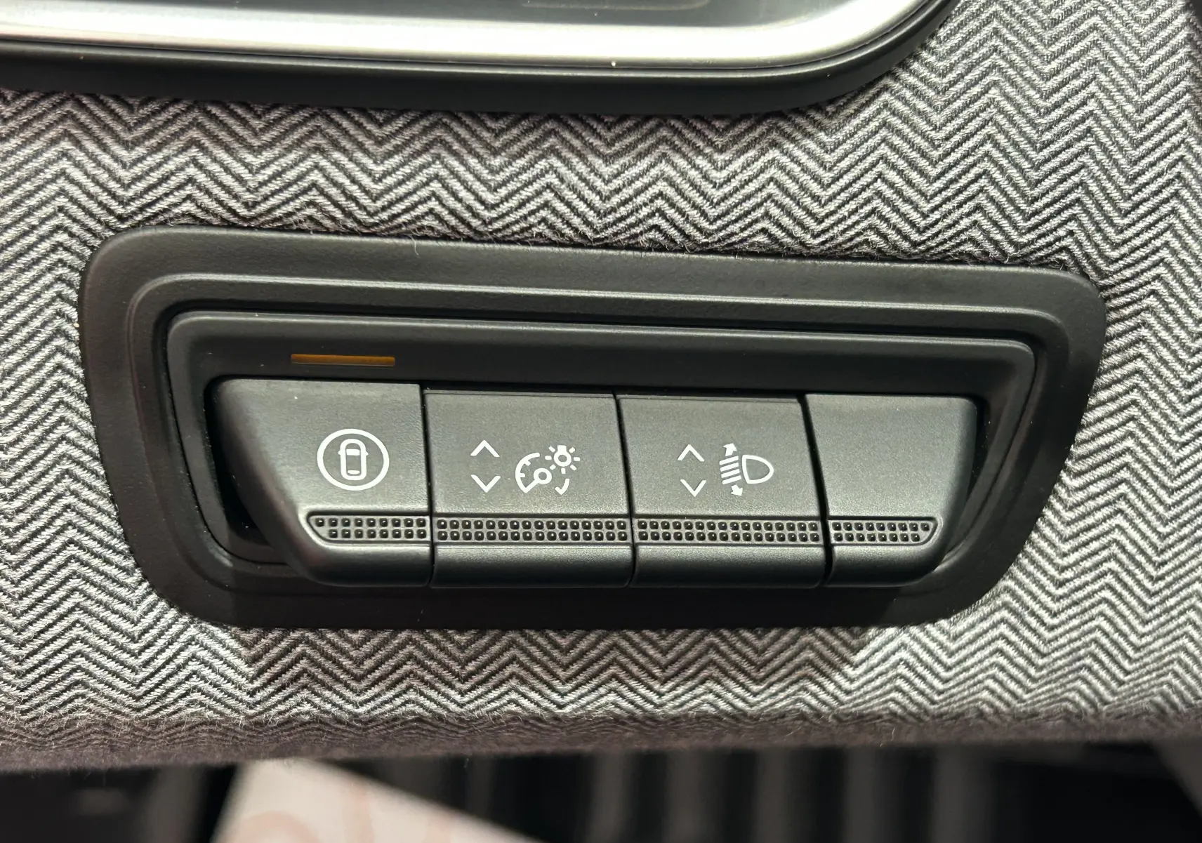 Gros plan sur les commandes de réglage des feux et verrouillage, sur tissu gris à motif chevrons dans une Renault Clio V bleu Iron Metal.