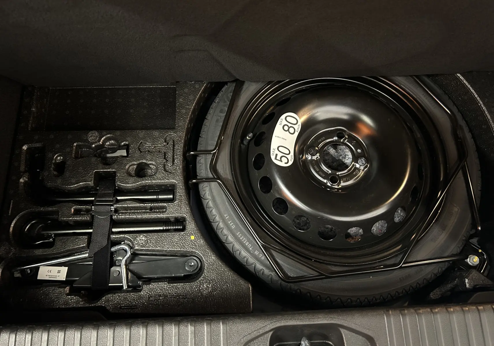 Vue en plongée sur la roue de secours et les outils de bord rangés dans le coffre d'une Renault Clio V bleu Iron Metal.