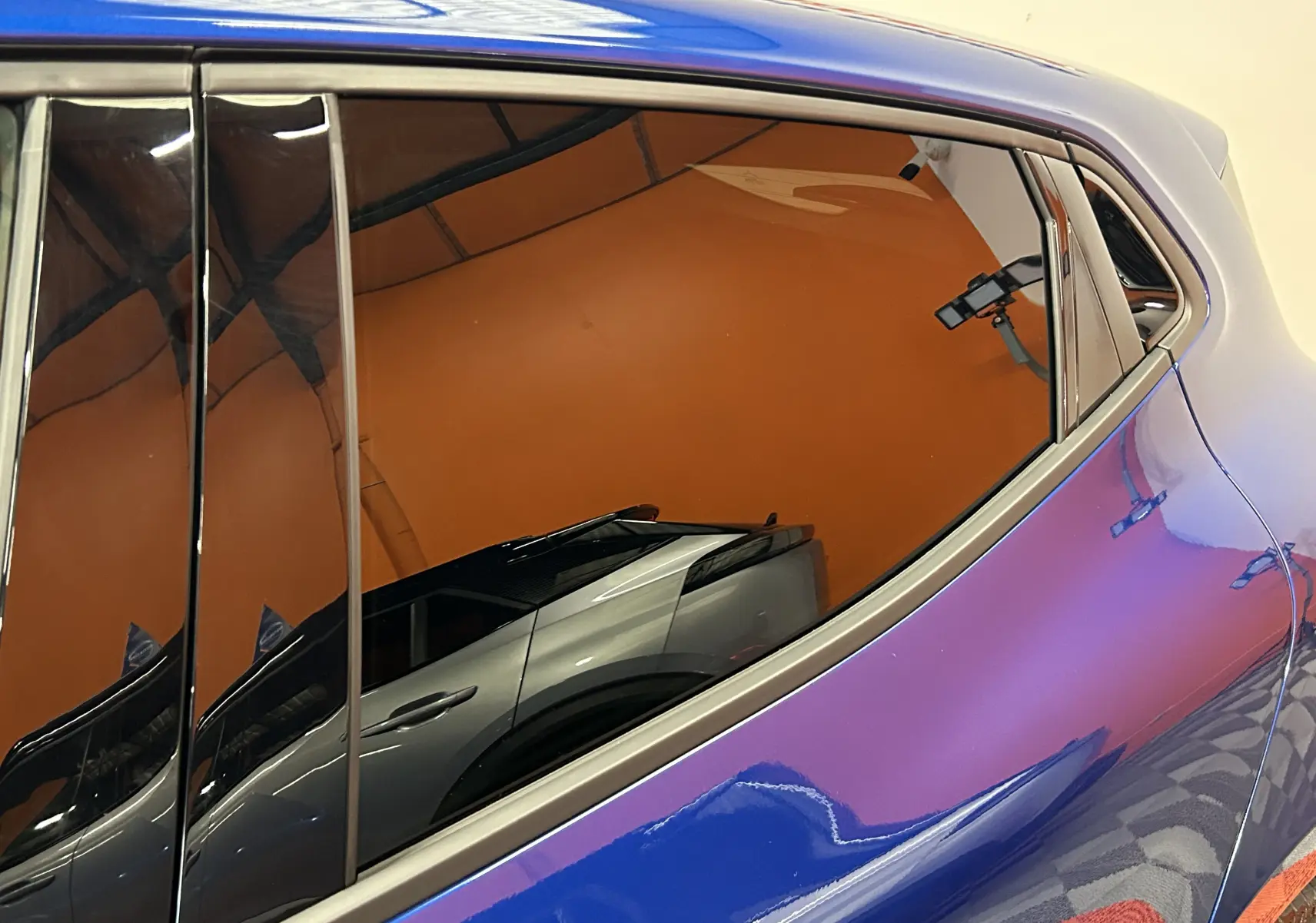 Détail de la vitre arrière droite d'une Renault Clio V bleu iron metal avec reflet d'un autre véhicule gris.