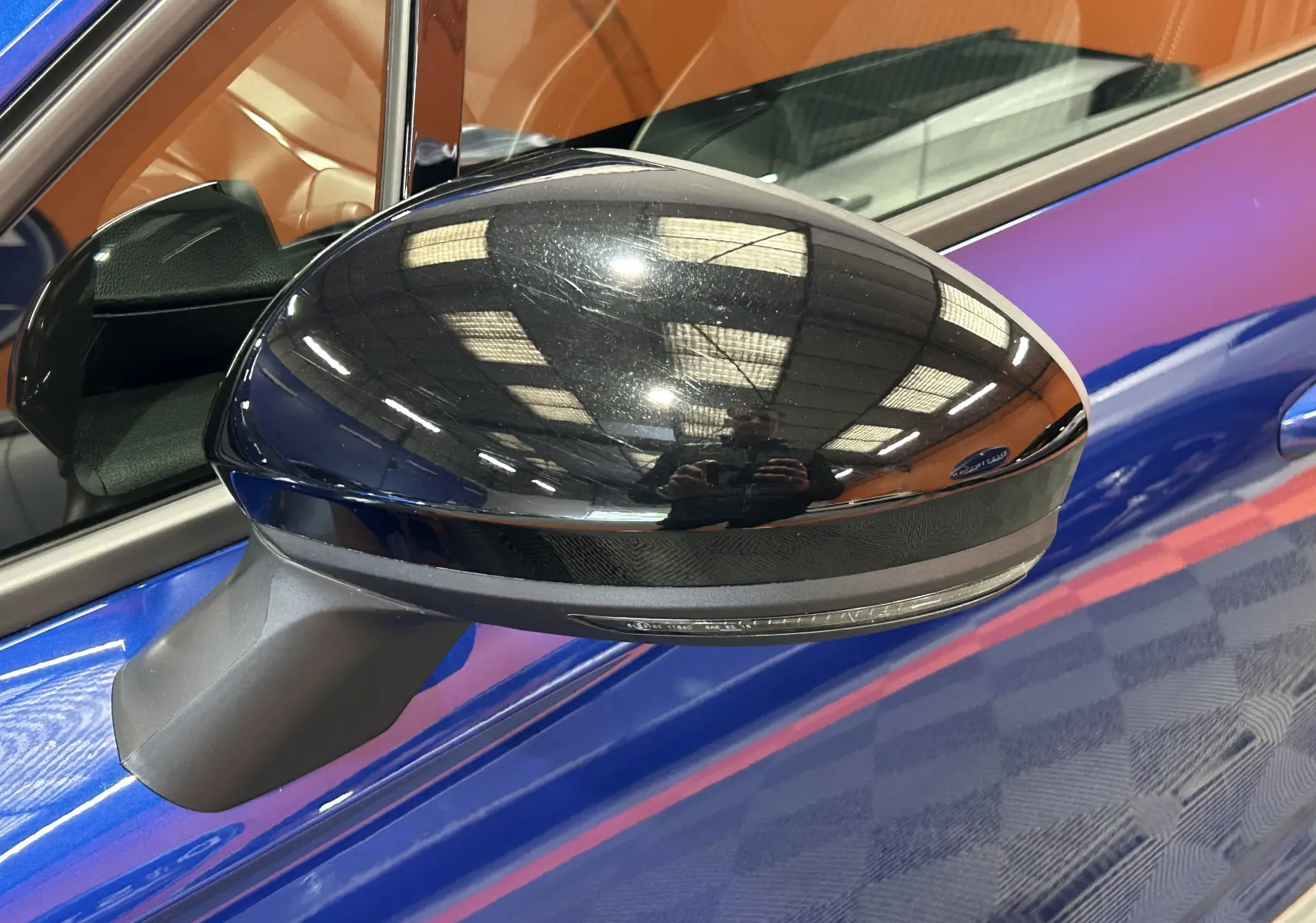 Rétroviseur noir brillant côté gauche d’une Renault Clio V bleu iron metal, avec reflet intérieur visible.
