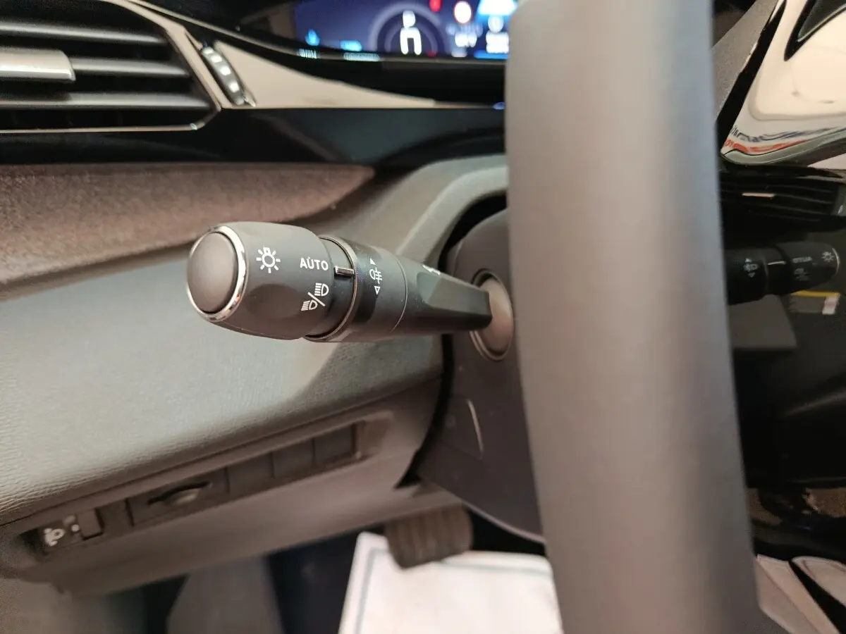 Gros plan sur la commande des phares à gauche du volant cuir dans l’habitacle de la Peugeot 308 gris foncé 2026.