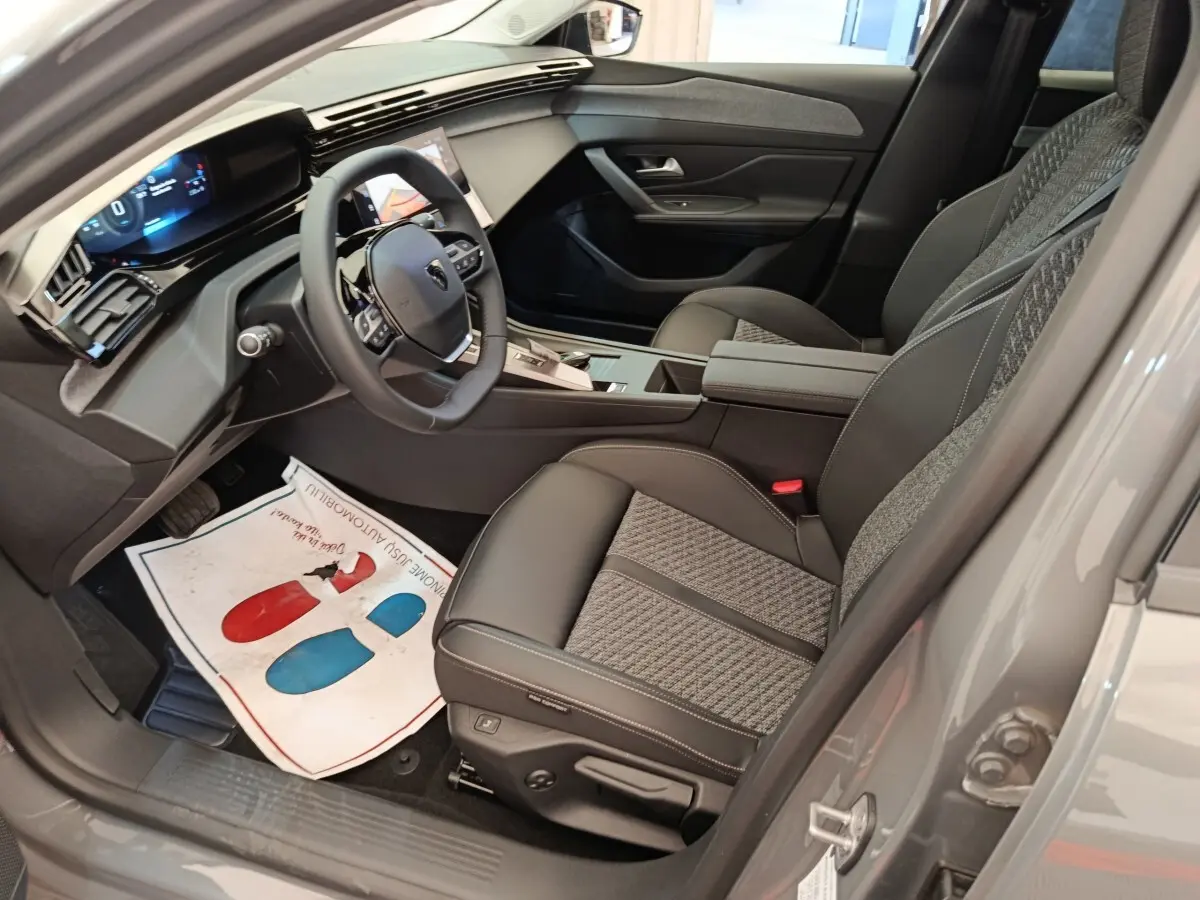 Intérieur avant droit de la Peugeot 308 gris foncé 2026, volant cuir multifonctions et sièges tissu/cuir bicolores.