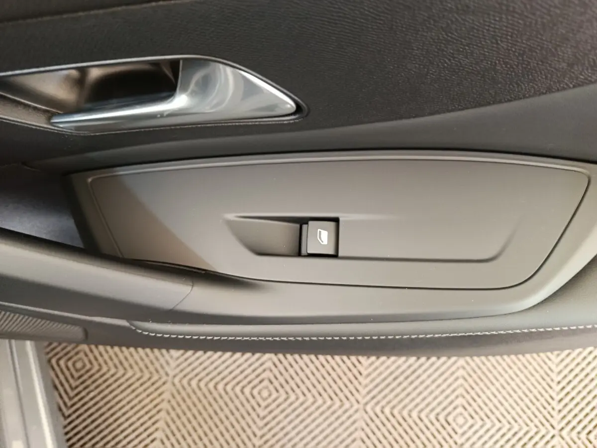 Gros plan sur la commande de lève-vitre côté conducteur de la Peugeot 308 gris foncé, intérieur moderne.