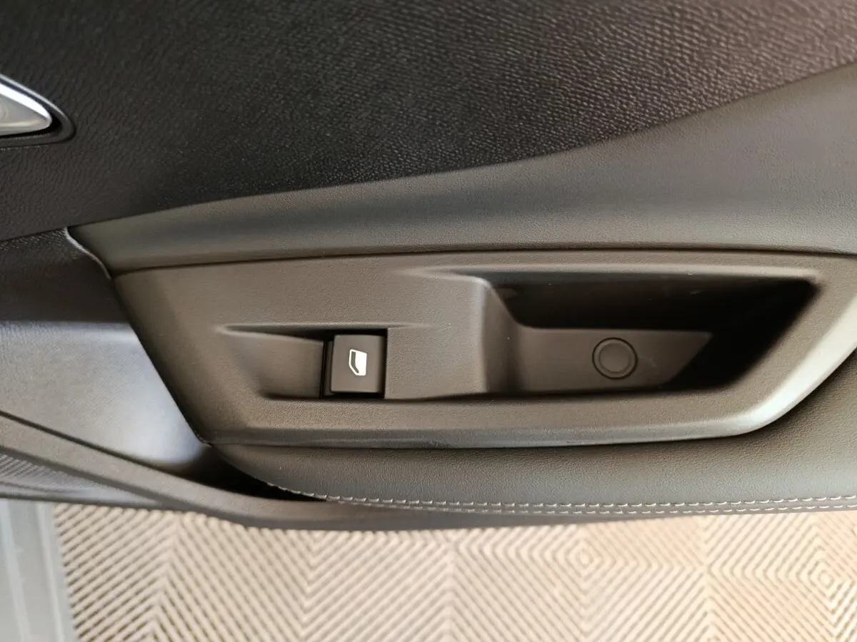 Gros plan sur la poignée intérieure de porte côté gauche d'une Peugeot 308 gris foncé, avec bouton de commande de vitre.