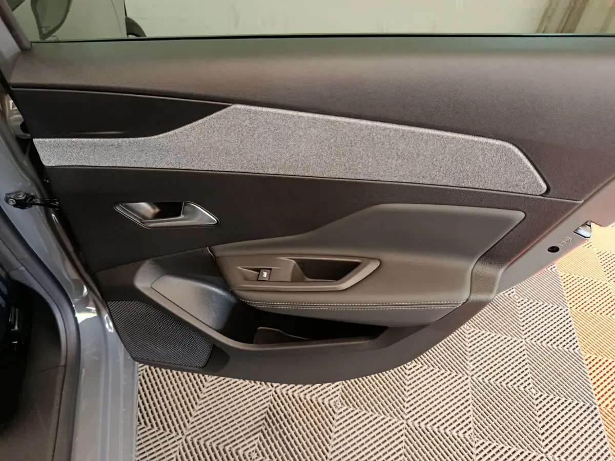 Vue intérieure côté gauche de la porte avant gris foncé de la Peugeot 308 2026 avec garniture tissu et commandes électriques.