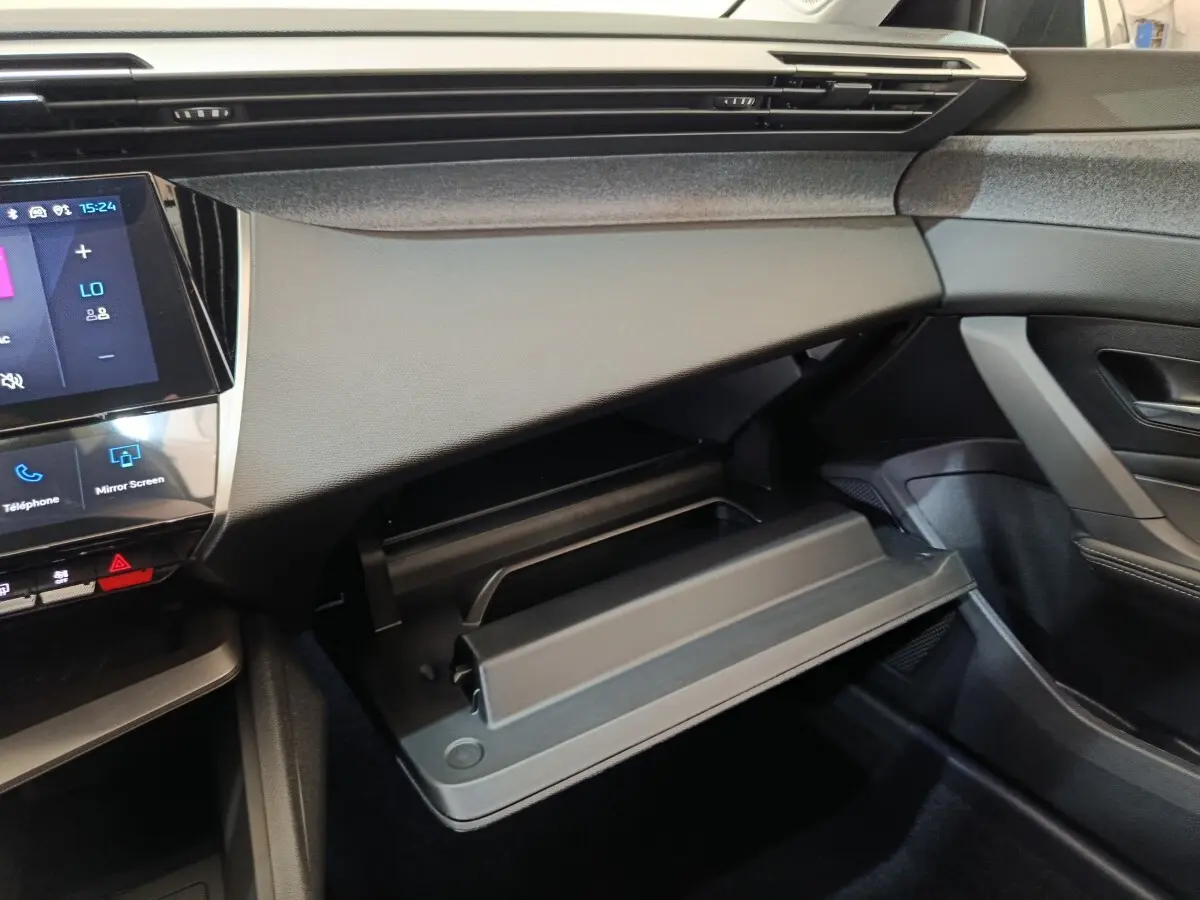 Intérieur Peugeot 308 BlueHDi 2026, vue côté passager sur boîte à gants ouverte et tableau de bord noir.