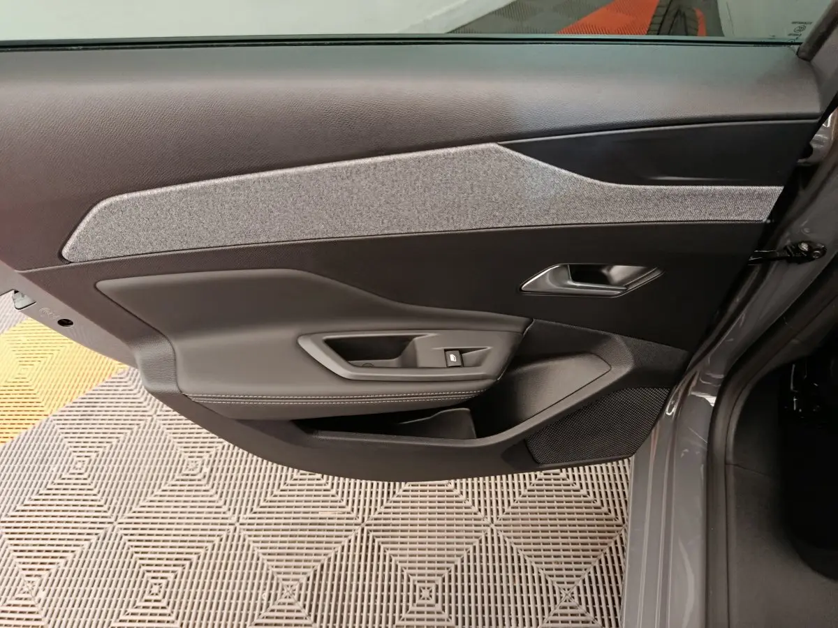 Vue intérieure de la porte avant droite gris foncé de la Peugeot 308 2026 avec habillage tissu et commandes électriques.