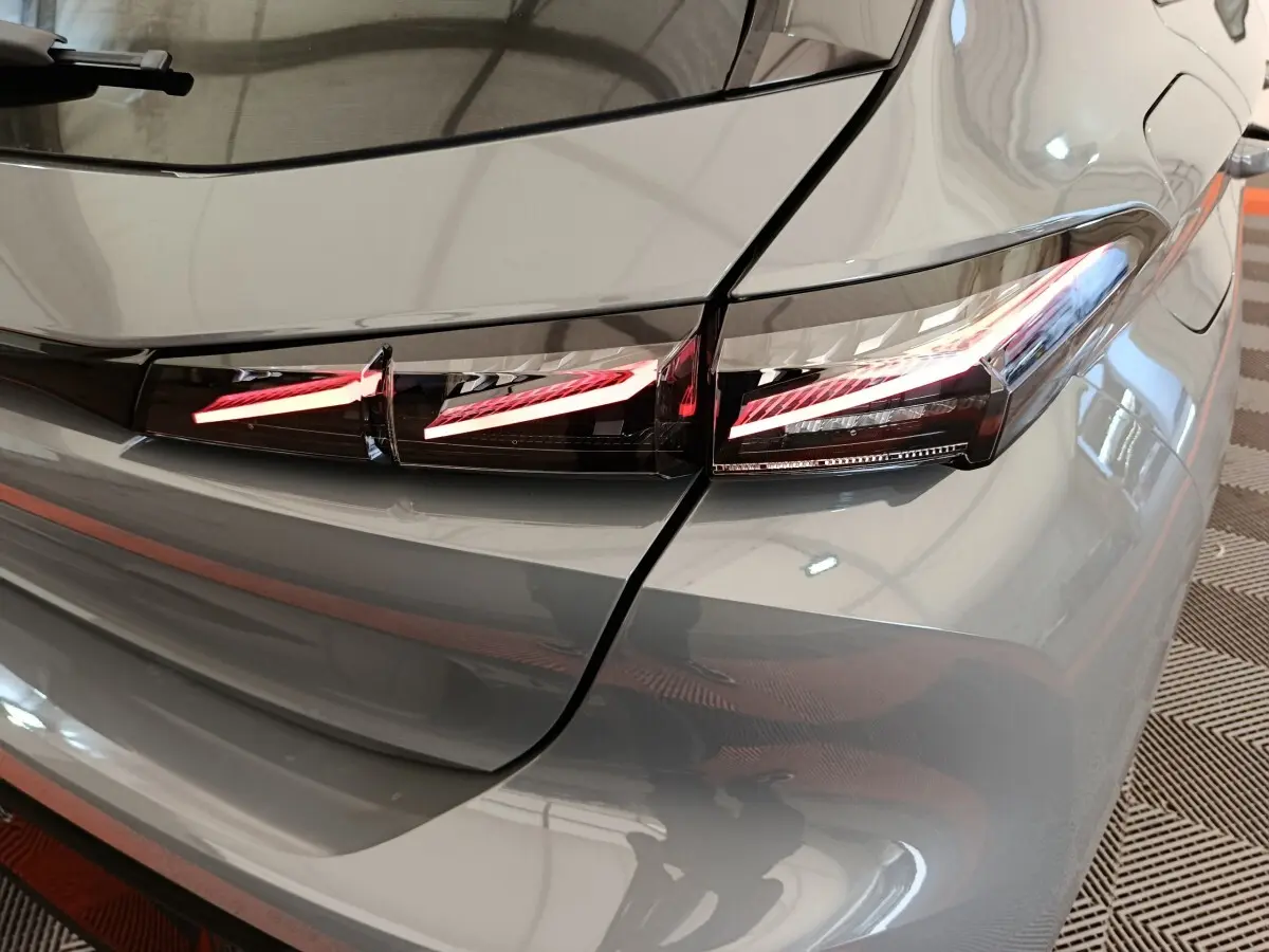 Feu arrière droit allumé en détail sur Peugeot 308 gris foncé, vue rapprochée du coin arrière du véhicule.