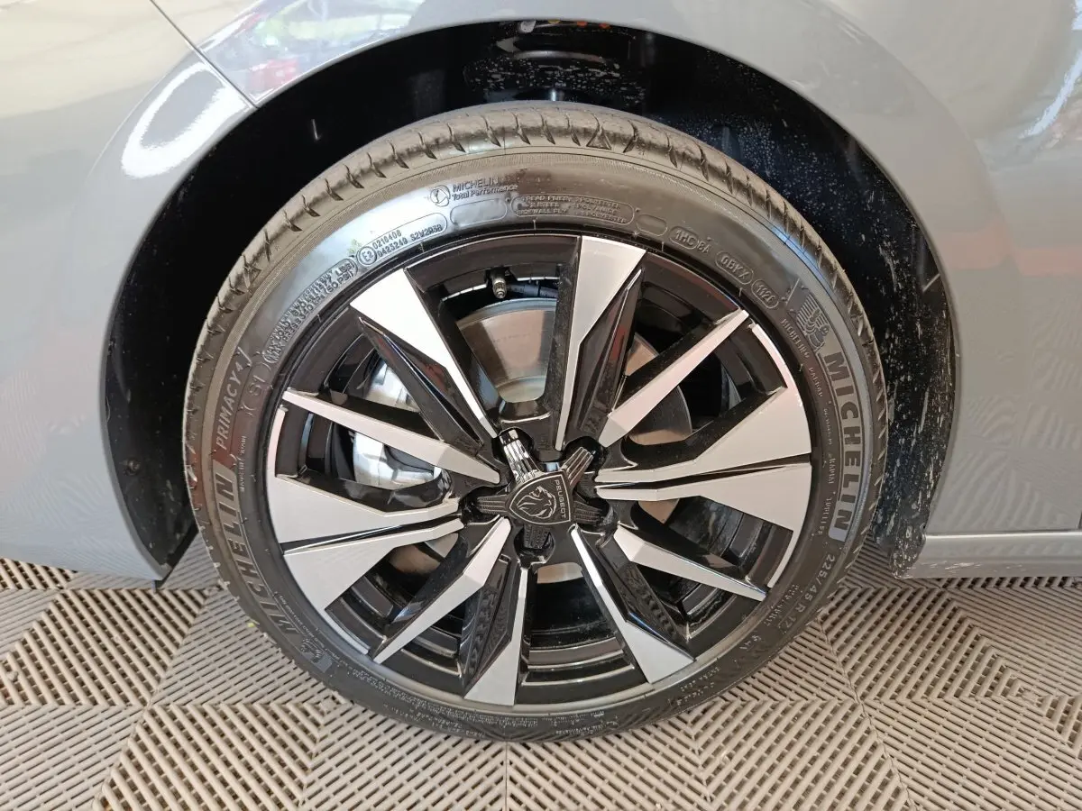 Gros plan sur la roue avant droite d'une Peugeot 308 gris foncé avec jante alliage bicolore et logo central Peugeot.