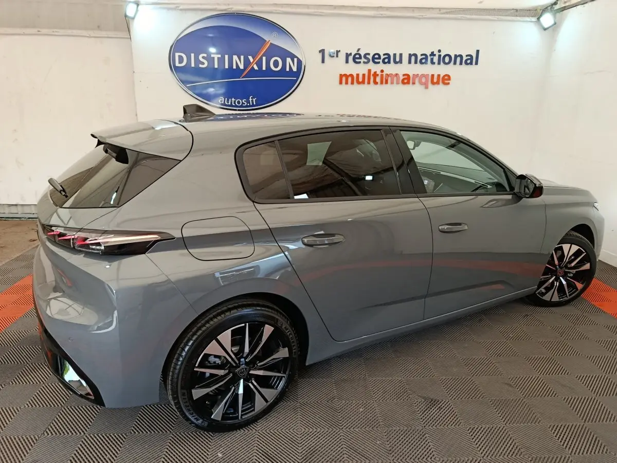 Peugeot 308 BlueHDi 130 en gris foncé, vue 3/4 arrière côté droit, avec jantes noires et feux LED distinctifs.
