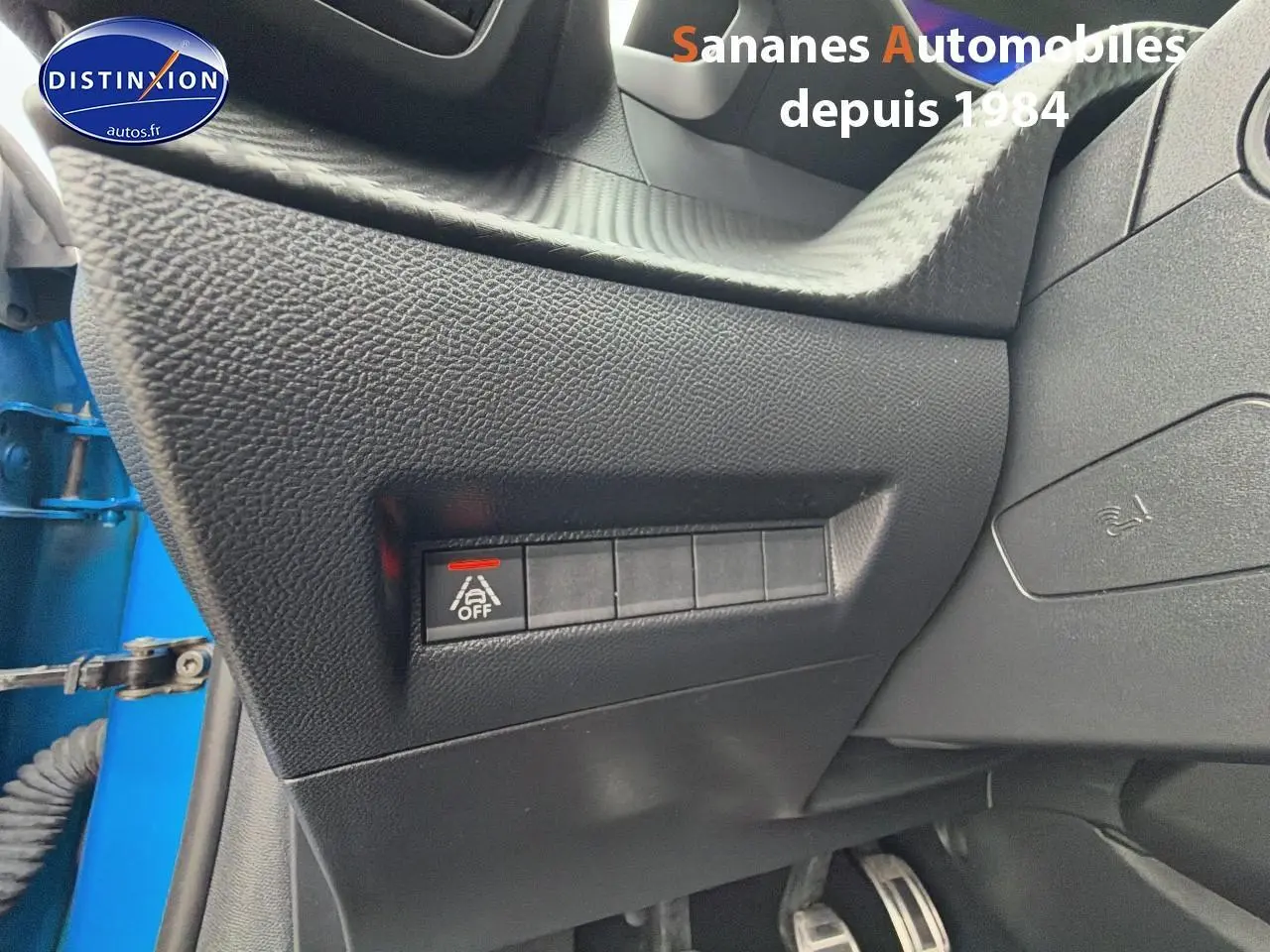 Gros plan sur la console côté gauche avec bouton désactivation assistance au maintien de voie, intérieur noir, portière bleu clair visible.