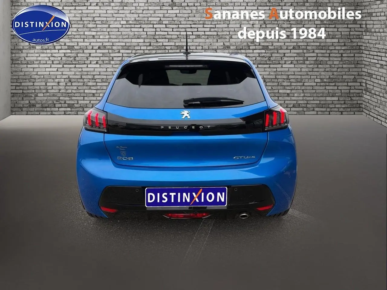 Vue arrière d'une Peugeot 208 GT Line bleu clair avec feux arrière LED et lunette teintée, sur fond gris et mur en briques.