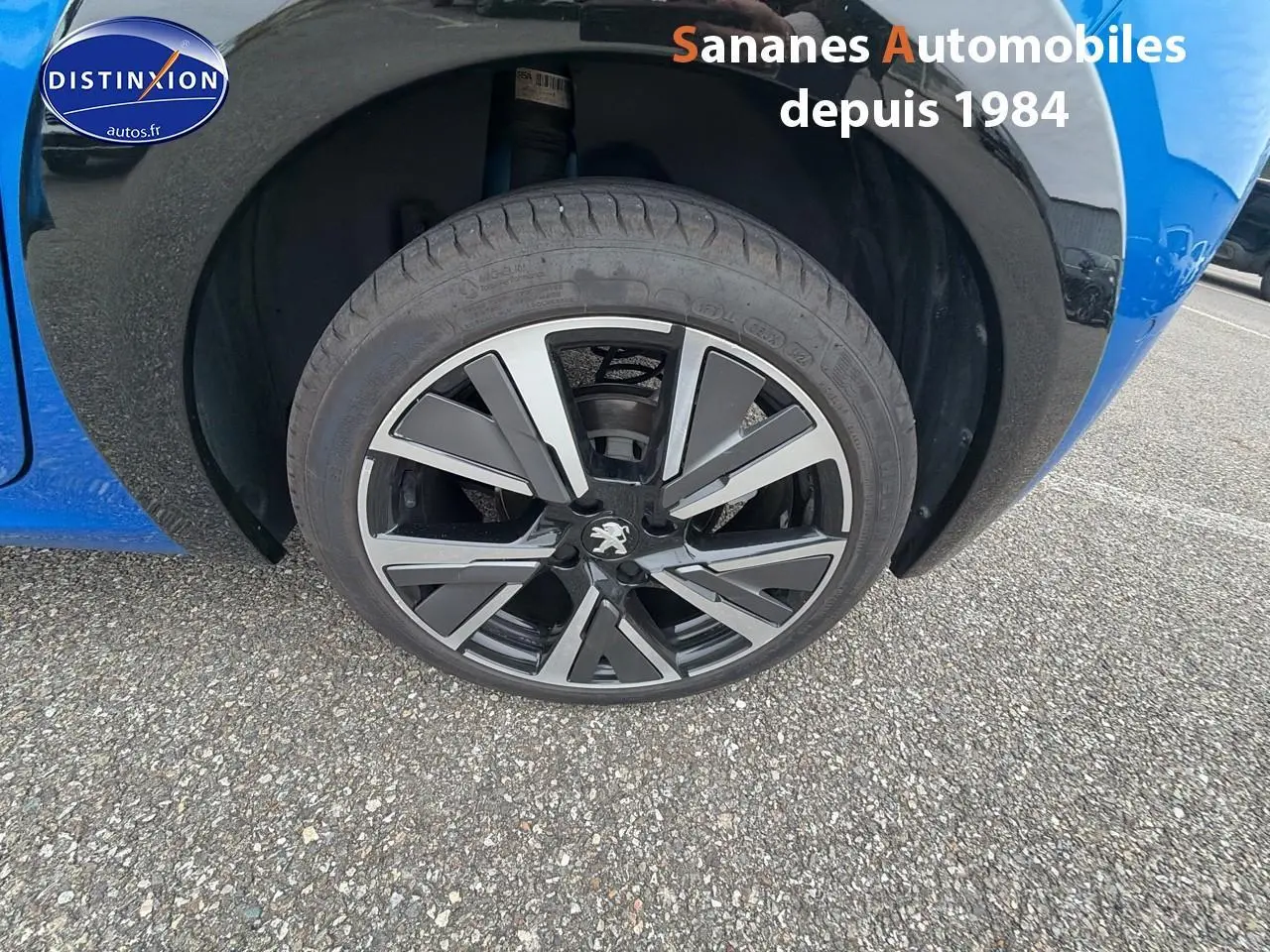 Gros plan sur la jante alliage noire et argentée du côté avant droit d'une Peugeot 208 bleu clair.