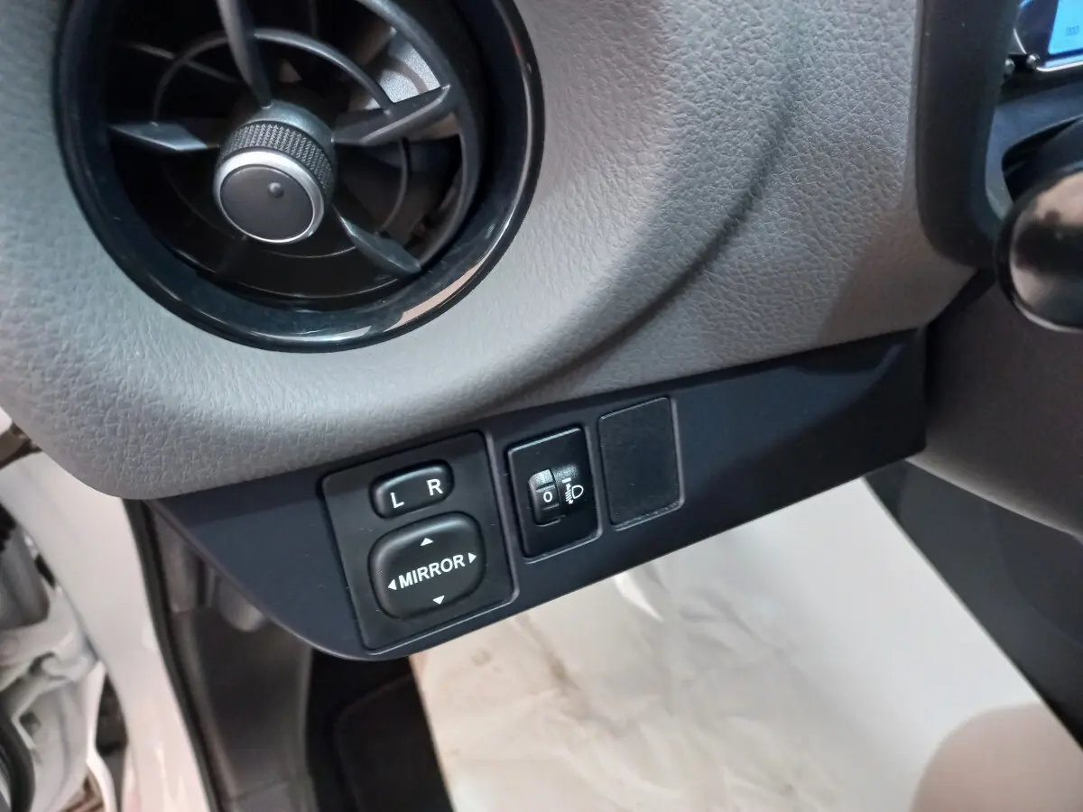 Gros plan sur commandes de réglage des rétroviseurs et ventilation côté conducteur de Toyota Yaris blanche 2019.