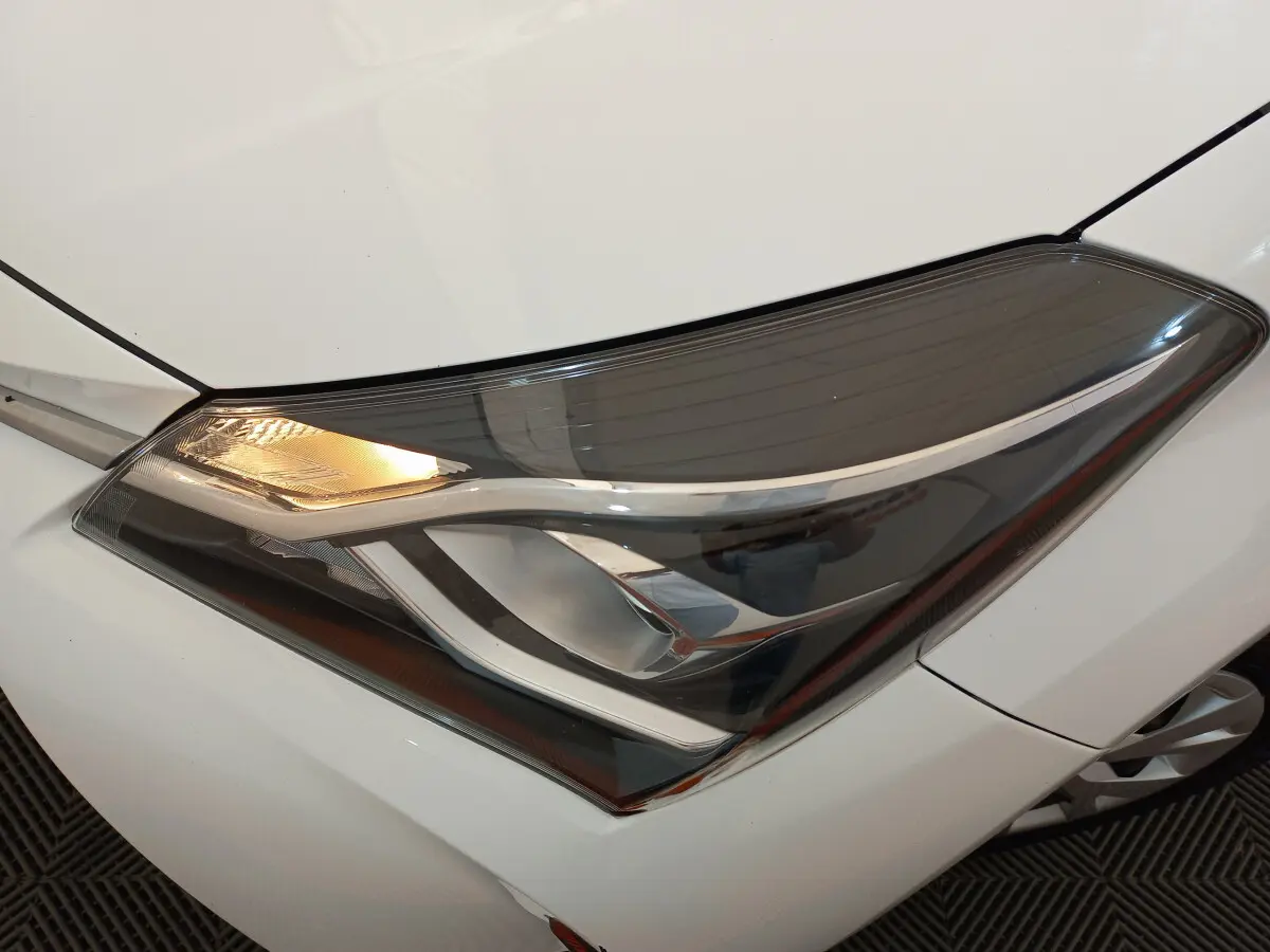 Gros plan sur le phare avant gauche allumé d'une Toyota Yaris blanche 2019, soulignant son design moderne et épuré.