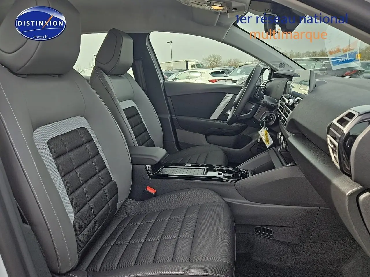 Vue intérieure côté conducteur de la Citroën C4 hybride 2025 avec sièges tissu noir et gris et console centrale noire brillante.